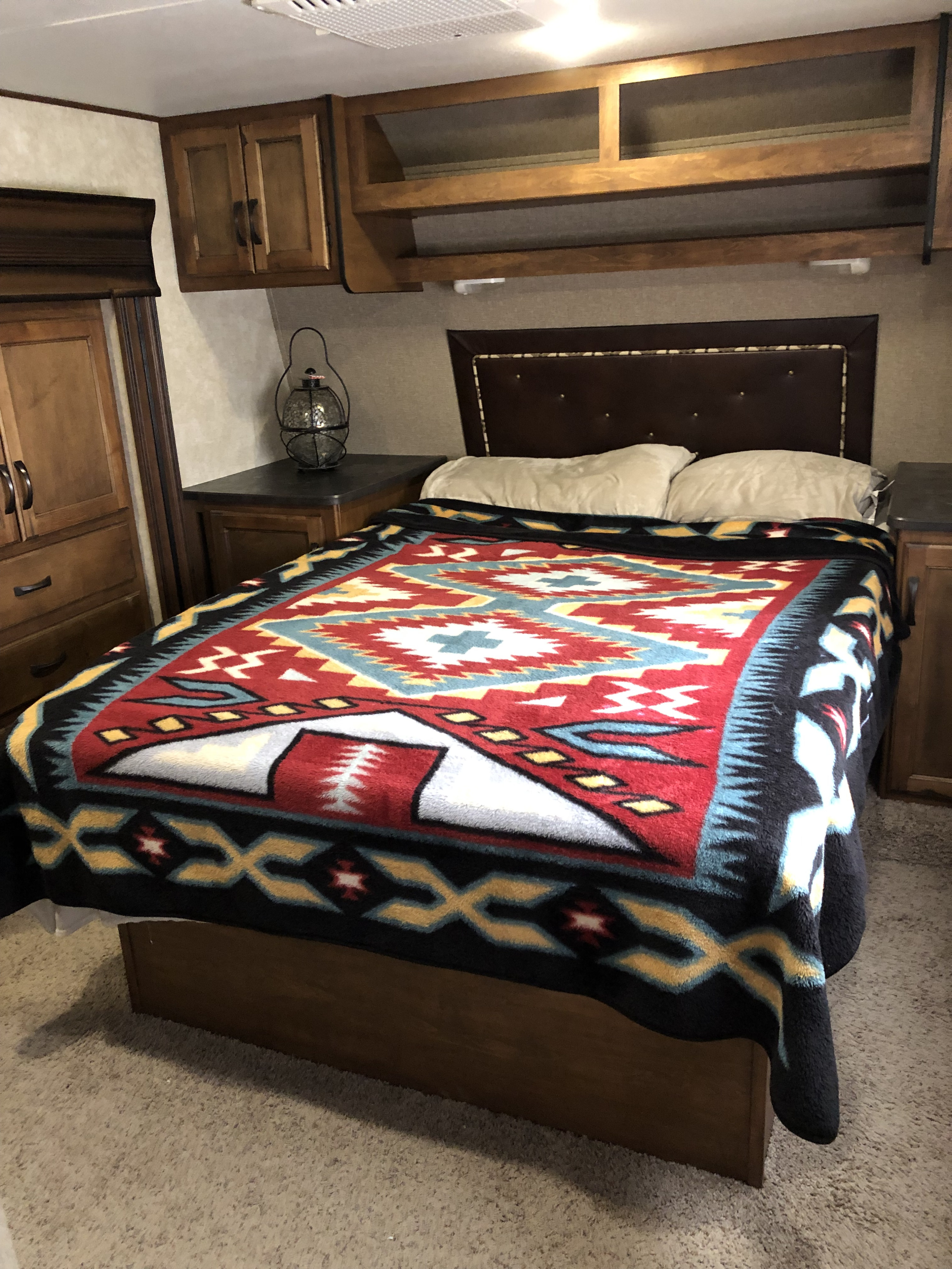 RV rental bedroom featuring a bed with a vibrant Southwestern-patterned blanket, brown headboard, and wooden cabinetry.. Keystone Carbon 2015