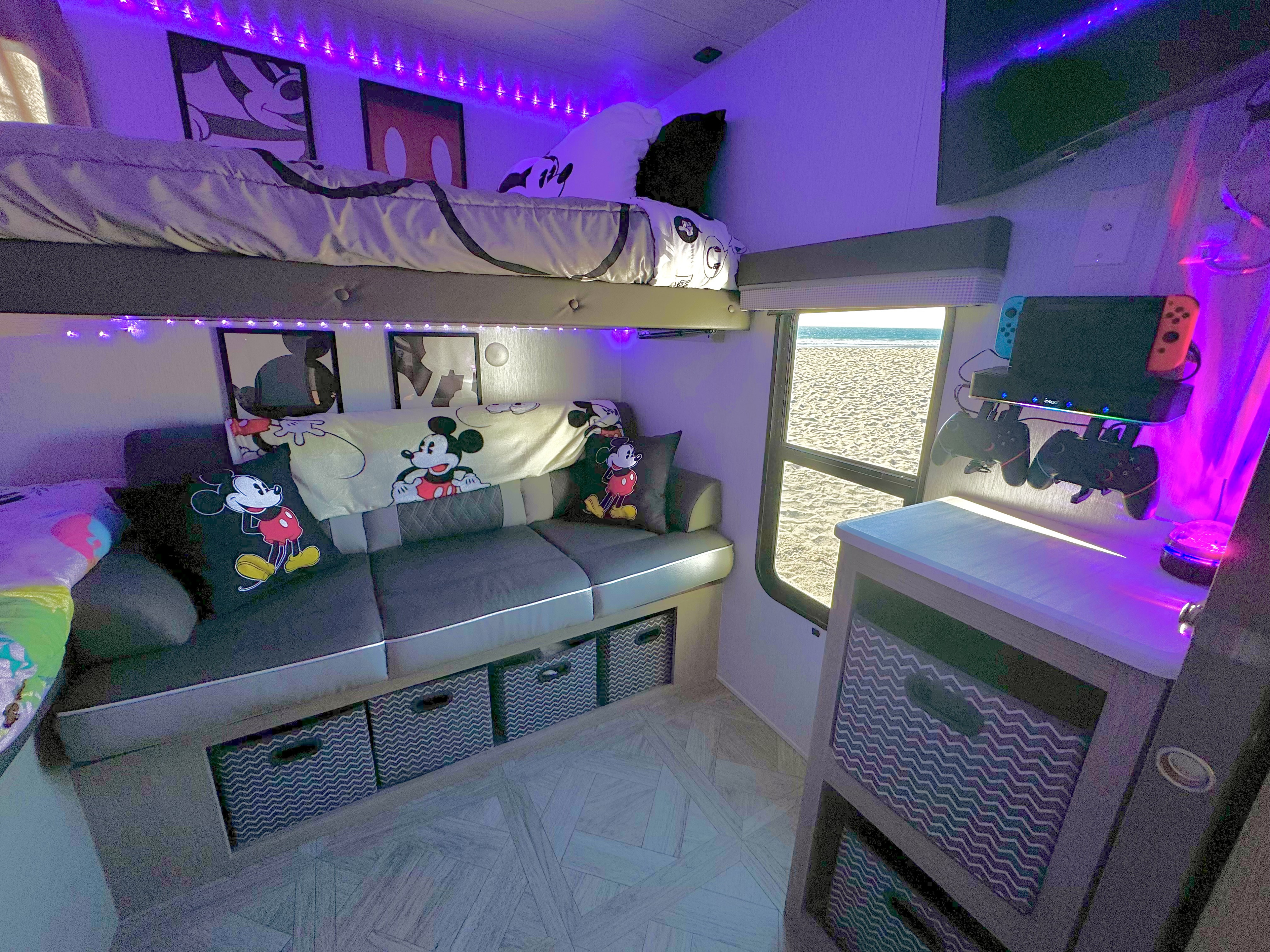 Cozy rv rental bunk and lounge area with Mickey Mouse decor, purple lights, a gaming setup, and beach view.. Forest River Wildwood 2024
