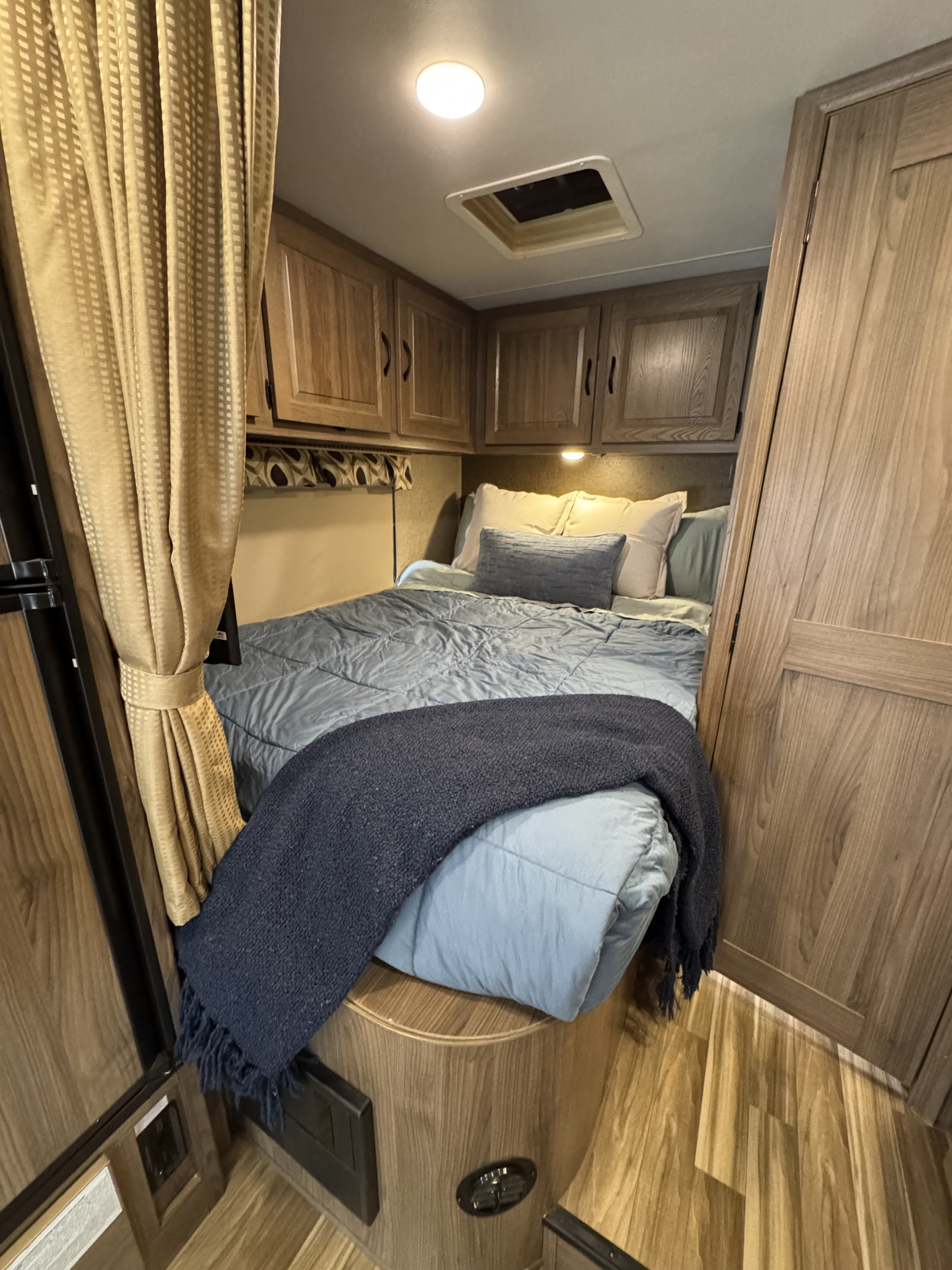 Cozy RV rental bedroom with light wood cabinetry, blue bedding, and a ceiling vent. All set for a comfortable stay.. Forest River Coachmen Prism 2017
