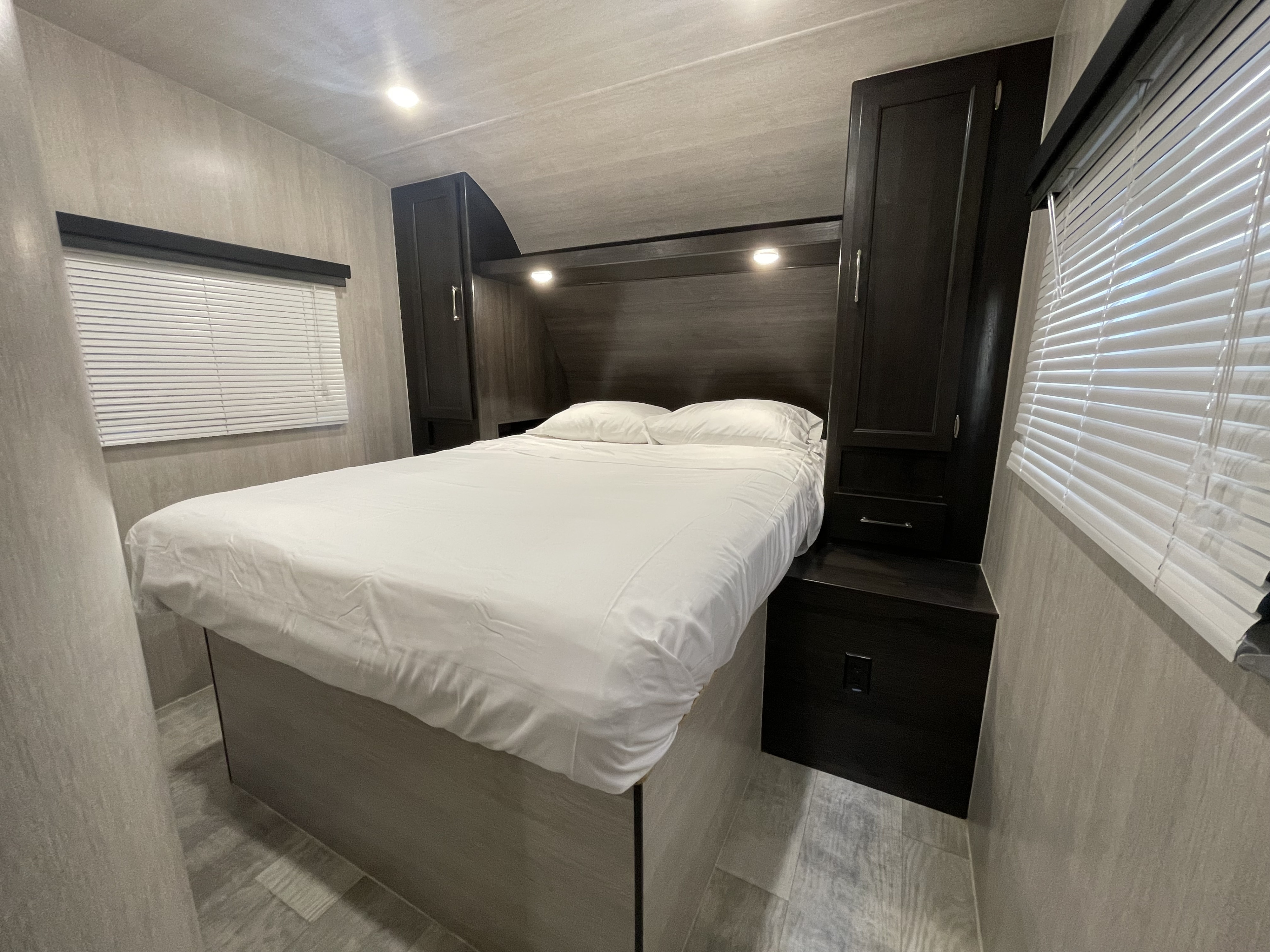 Comfortable RV rental bedroom with a white bed, dark wood cabinets, and window blinds. Ideal for your next journey.. Pacific Coachworks Sandsport 2022