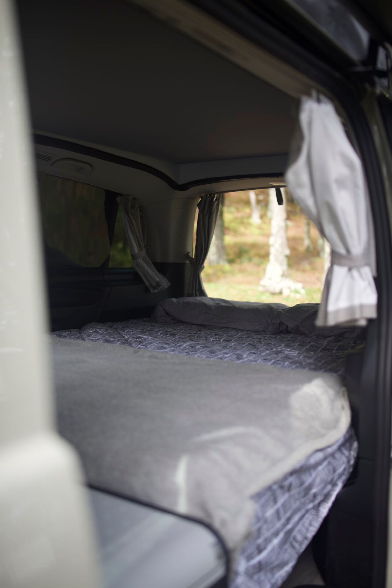 A comfortable bed inside an RV rental, offering serene nature views. Perfect for a cozy camping trip.. Mercedes Metris 2021