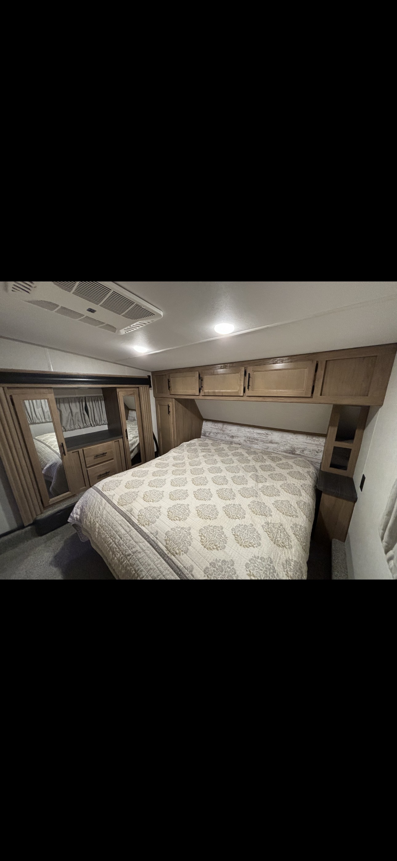 Spacious RV rental bedroom with comfortable bed, overhead cabinets, and mirrored closet. Ideal for travel.. Forest River 365 wolf pack toy hauler 2024