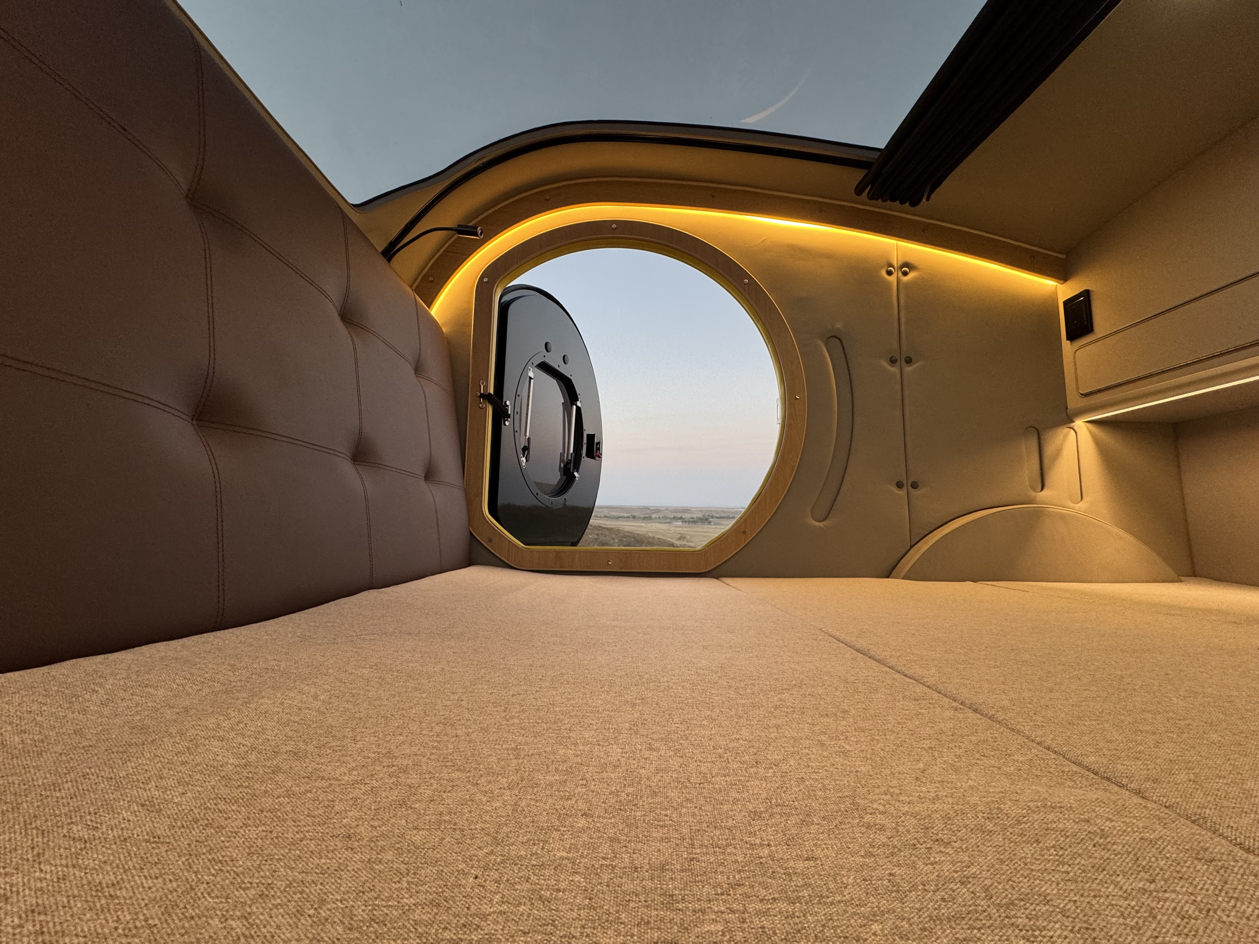 Comfortable RV rental interior with a large circular window and overhead skylight, offering a serene view and ambient lighting.. Hebei On The Road Comma-E 2024