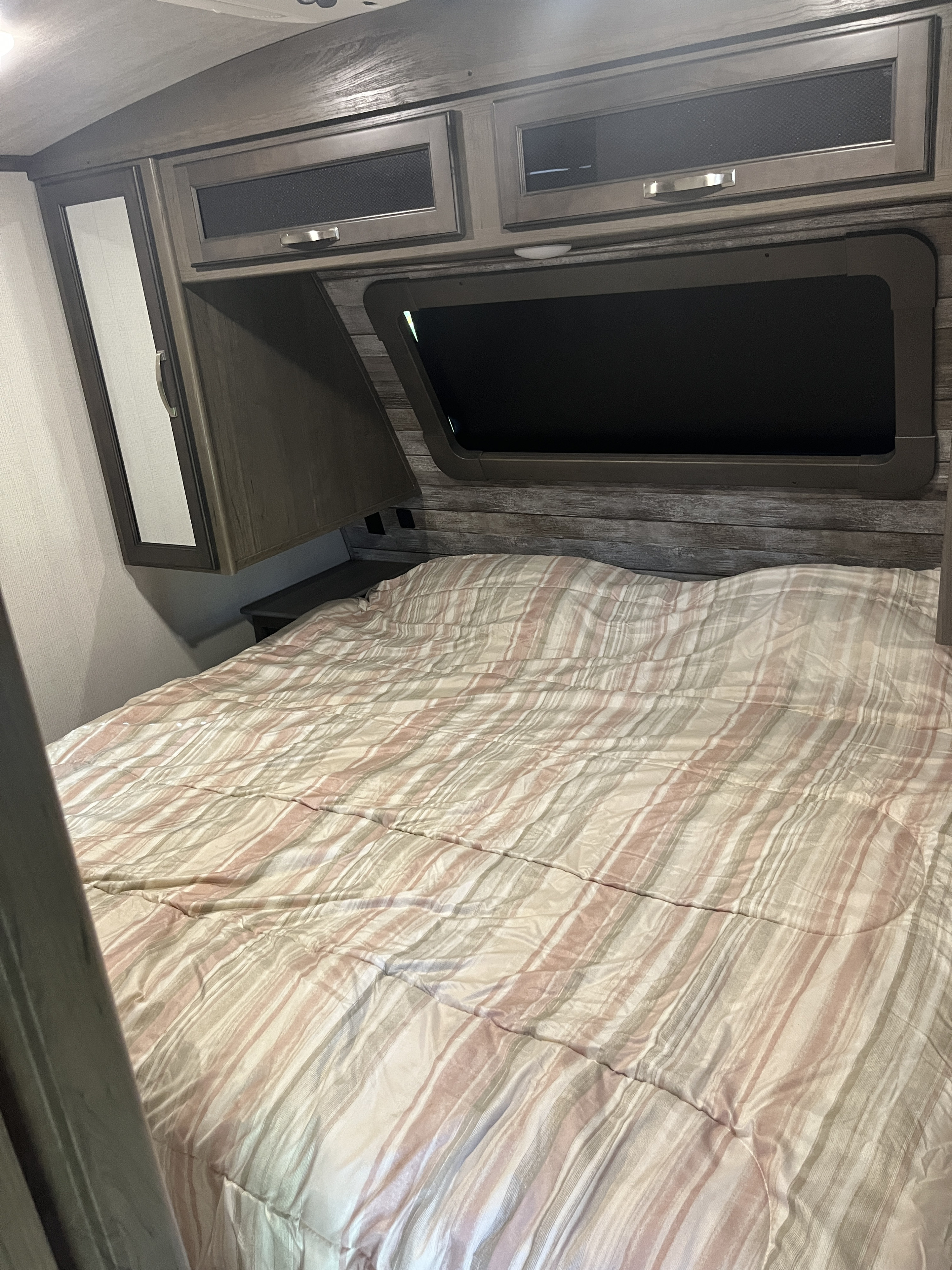 RV rental: RV bedroom with striped bed, overhead cabinets, window, and mirrored wardrobe for storage.. Keystone RV Cougar 2021