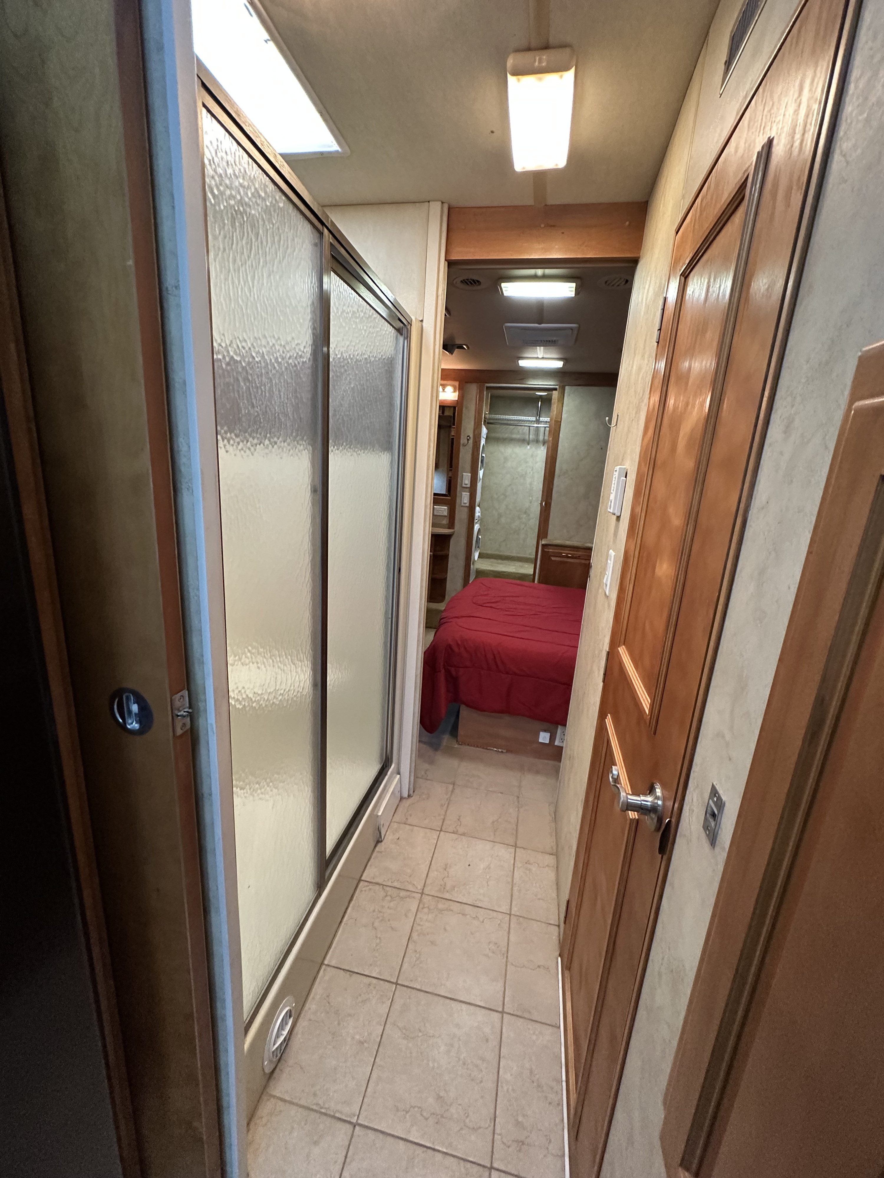 RV rental interior: View of a compact RV hallway with a shower stall on the left, leading to a bedroom with a red bed.. Gulf Stream Tour Master 2007