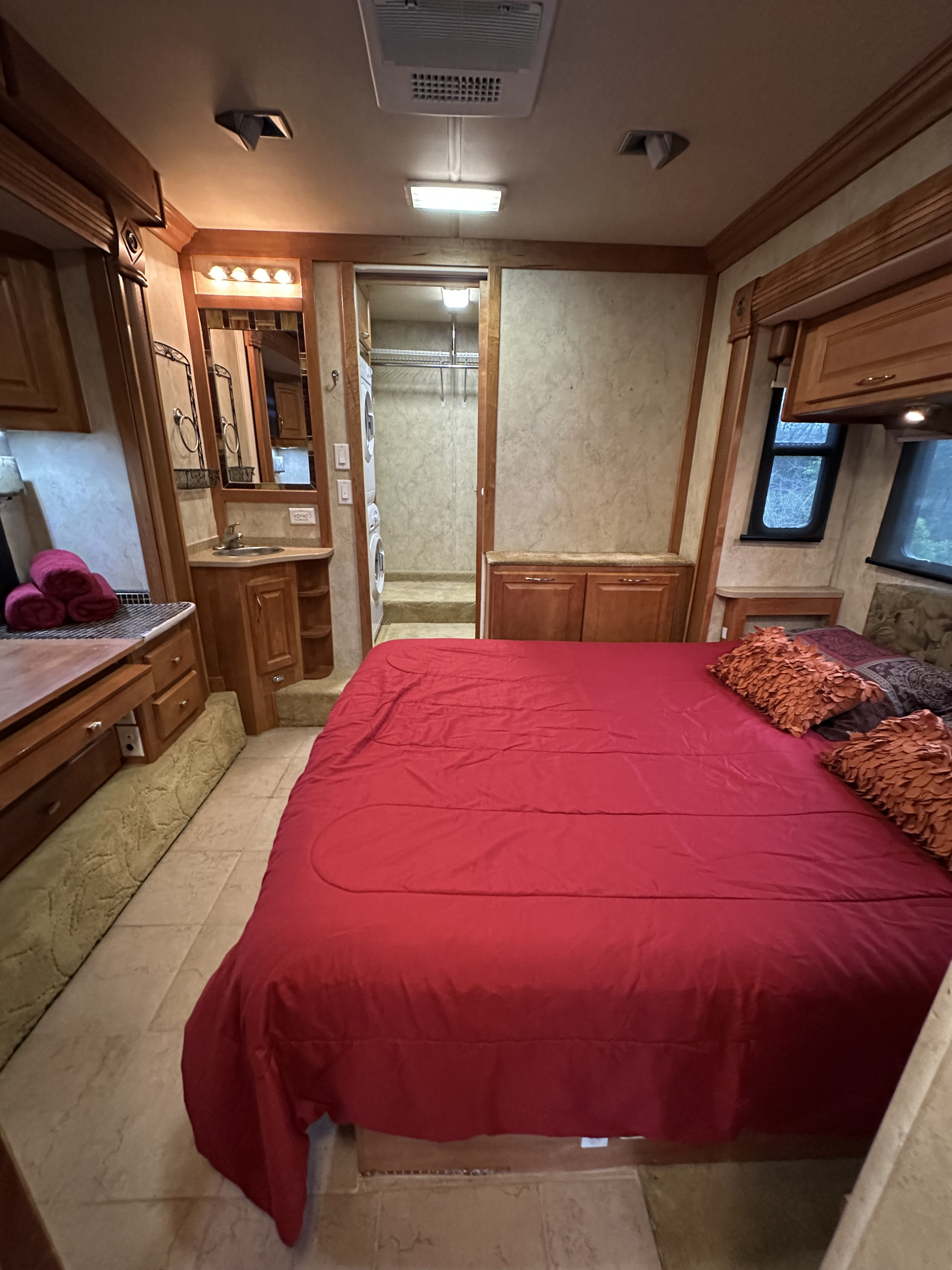 Spacious RV rental bedroom with a large red bed, adjacent vanity, and integrated laundry area for ultimate comfort.. Gulf Stream Tour Master 2007
