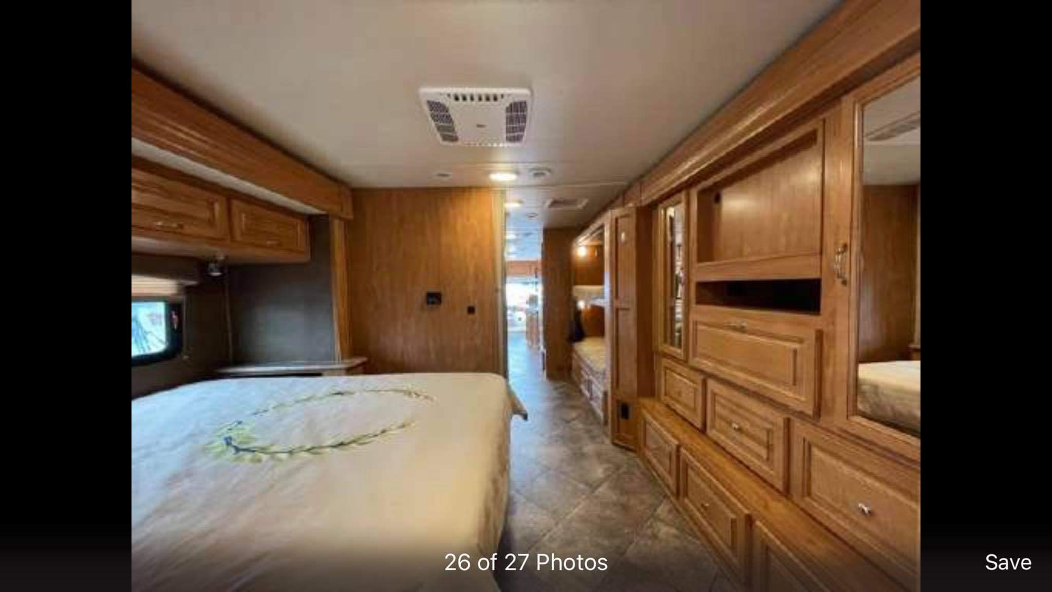 Spacious RV rental bedroom with a bed, overhead storage, built-in wood cabinets, and an aisle leading deeper into the unit.. Nexus RV Maybach 2018