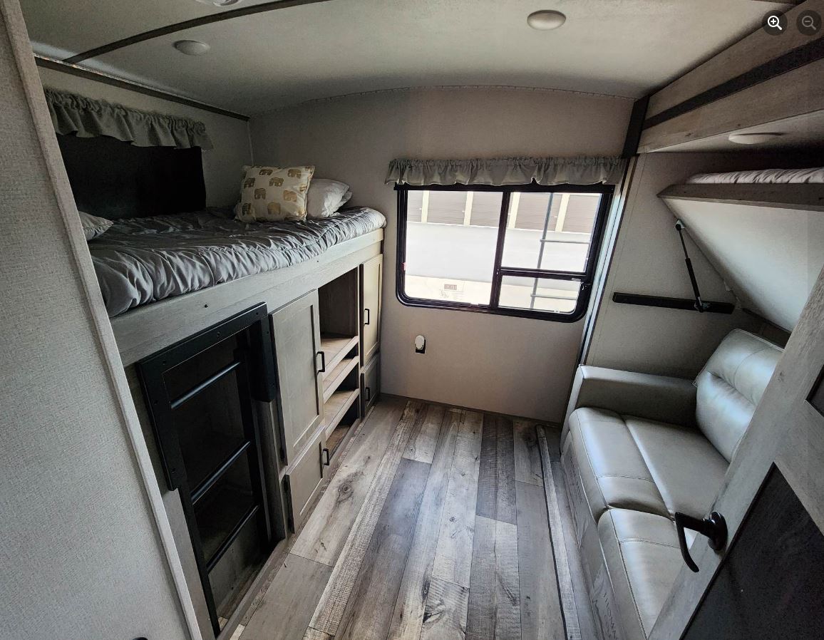 RV rental interior: A cozy space with a lower bunk bed, a sofa, and built-in storage on wood-look floors.. Keystone Outback 2021