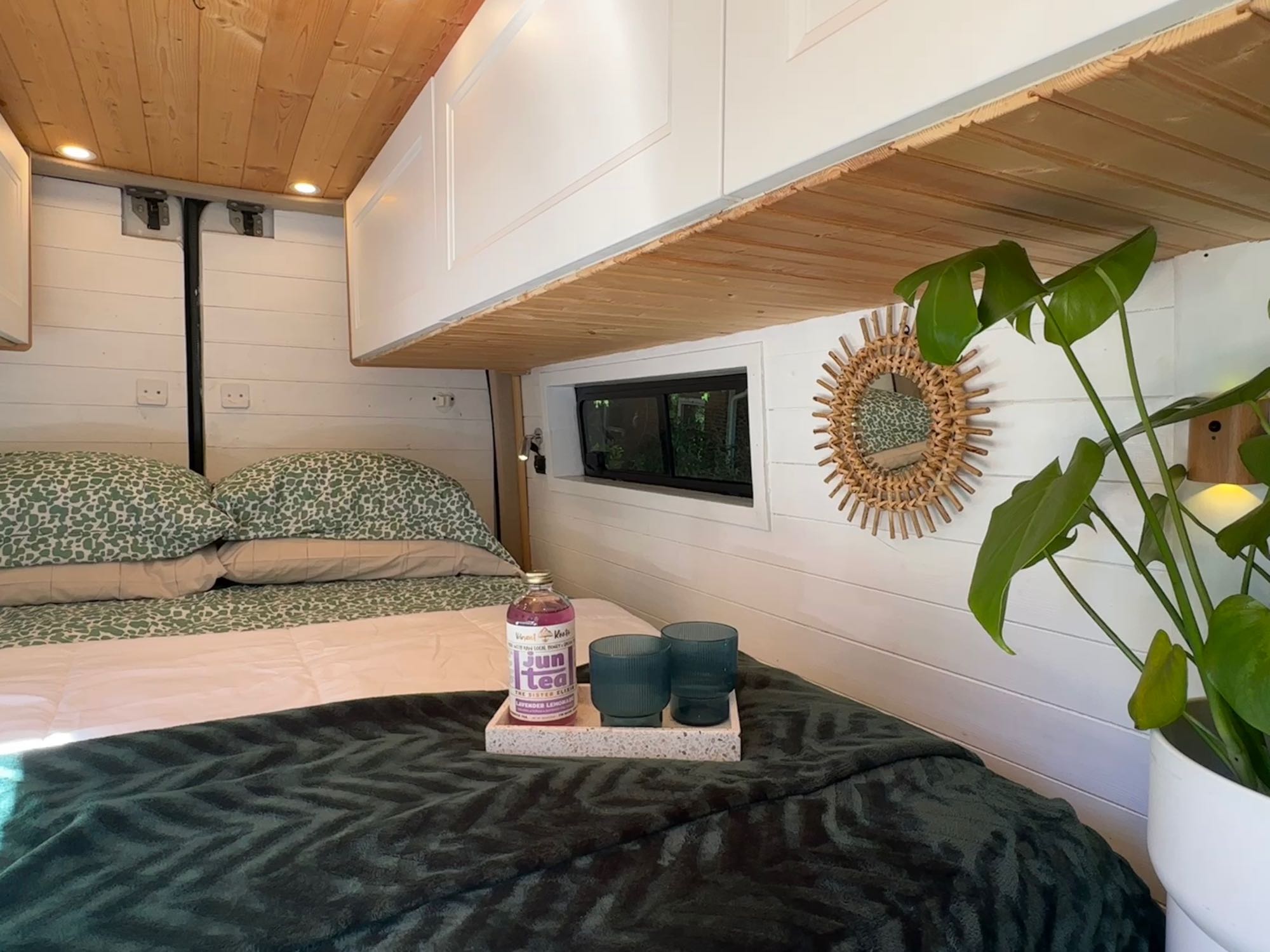 Cozy RV rental bedroom with a comfy bed, white paneled walls, and a warm wooden ceiling, featuring a plant & drink tray.. Mercedes Sprinter 2007