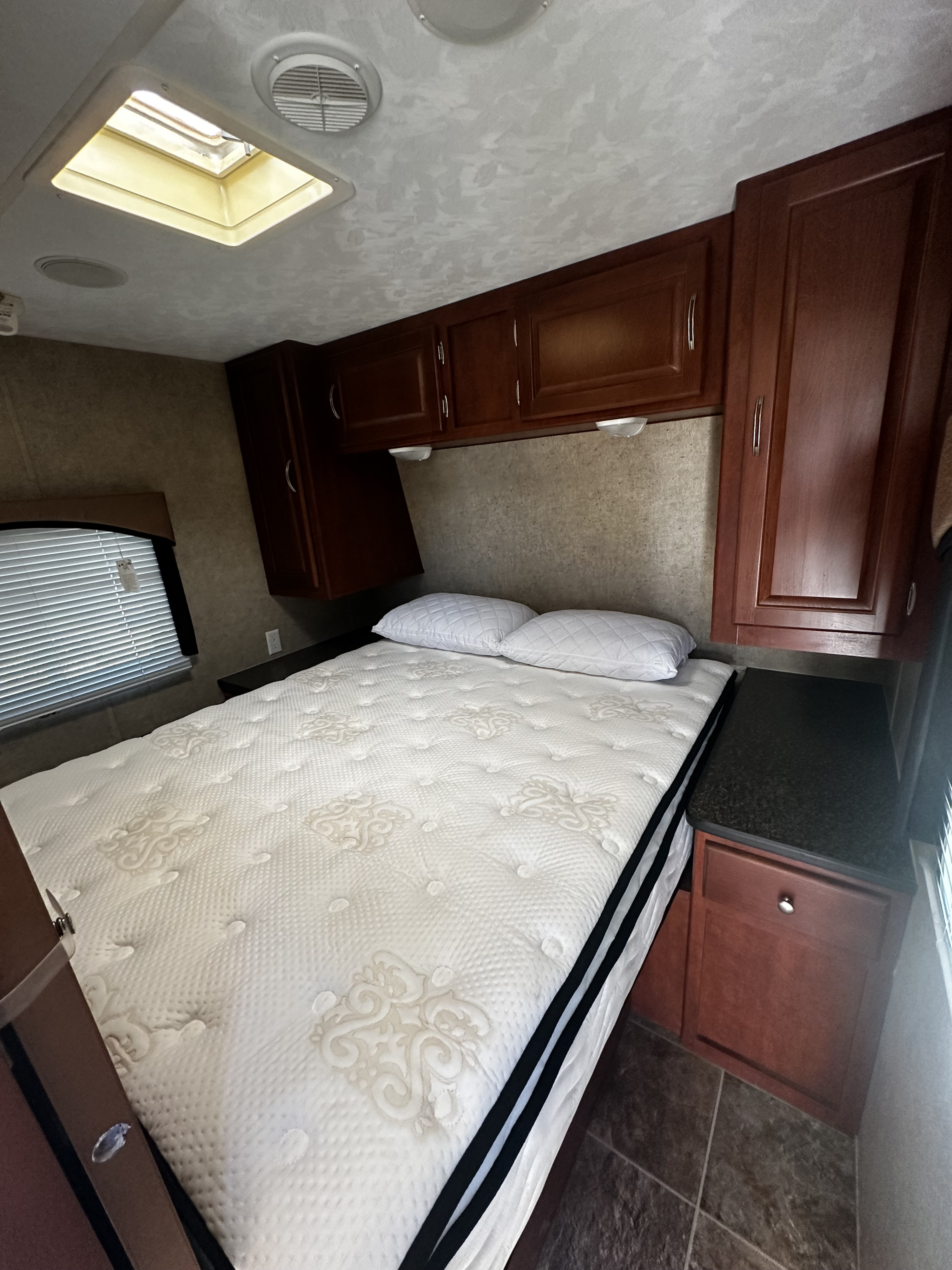 RV rental bedroom: comfortable bed with white mattress, dark wood overhead cabinets, window, and bright skylight.. Forest River Wildwood 2012