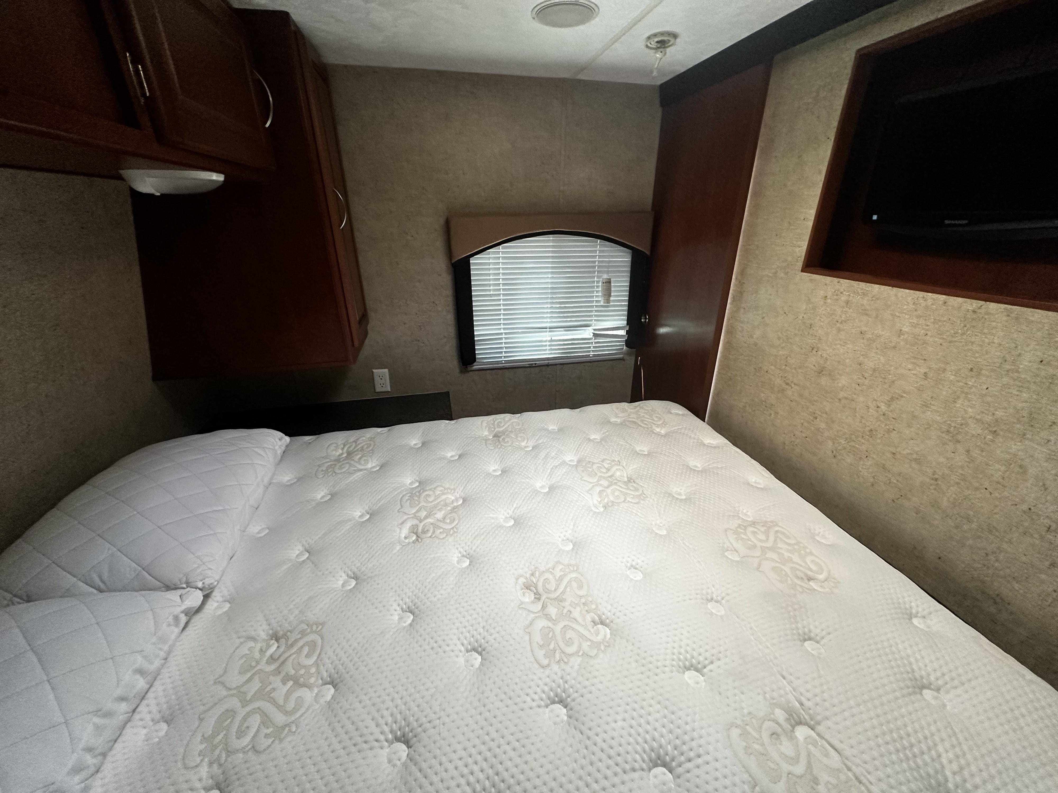 Cozy RV rental bedroom with a white mattress, wooden cabinets, a window, and a wall-mounted TV.. Forest River Wildwood 2012