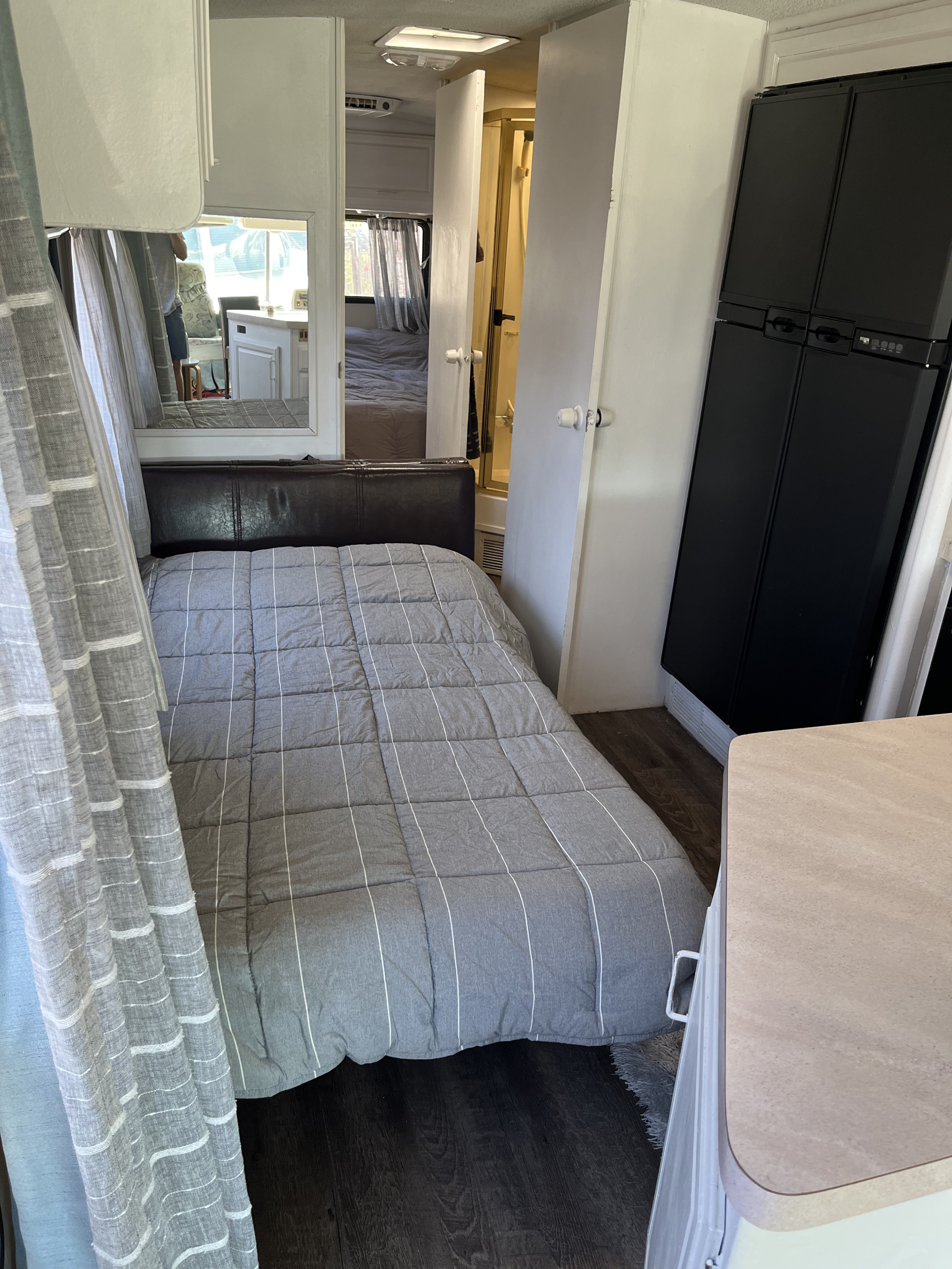RV rental interior: a bedroom with grey bedding, dark floor, mirrored wall, plus kitchen and fridge in a compact layout.. Fleetwood Bounder 1995