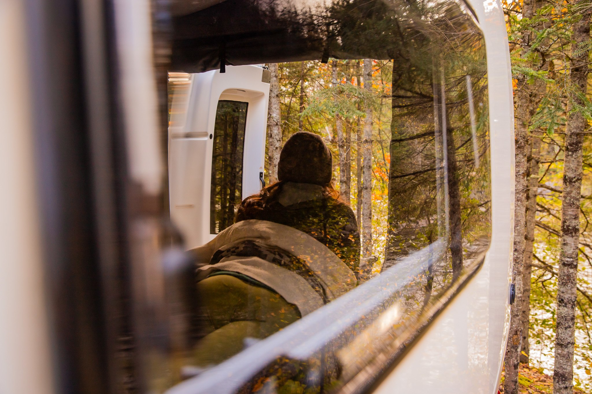 A person is seen from behind, looking out the large back window of an RV rental at a vibrant autumn forest.. Gmc sierra 1500 2024