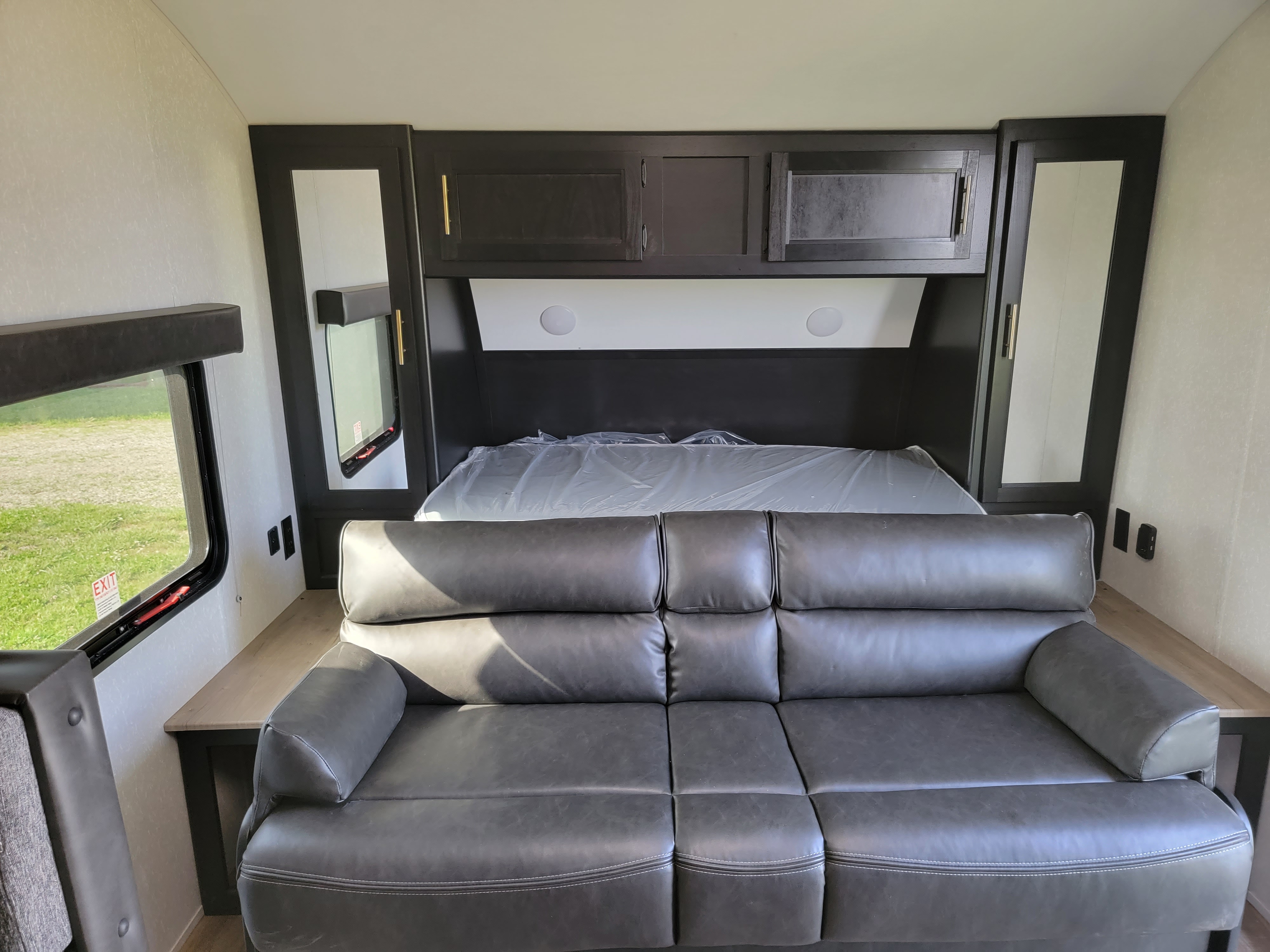 A clean RV rental interior features a grey leather sofa, an unused bed in plastic, and ample overhead storage.. Forest River Cherokee Grey Wolf 2022