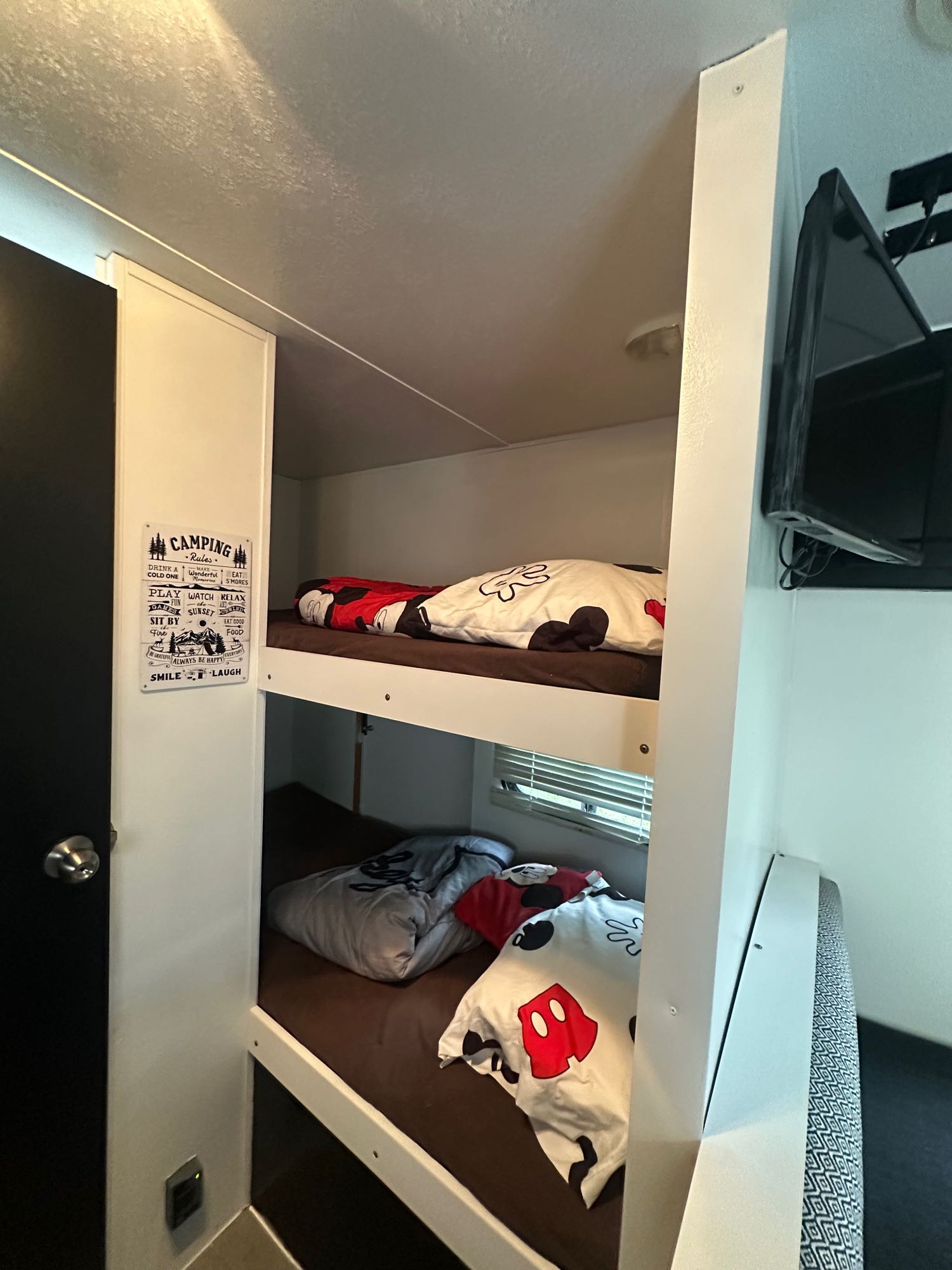RV rental bunk beds: Cozy sleeping area with Mickey Mouse bedding, a "Camping Rules" sign, and mounted TV.. Keystone Hideout 2016