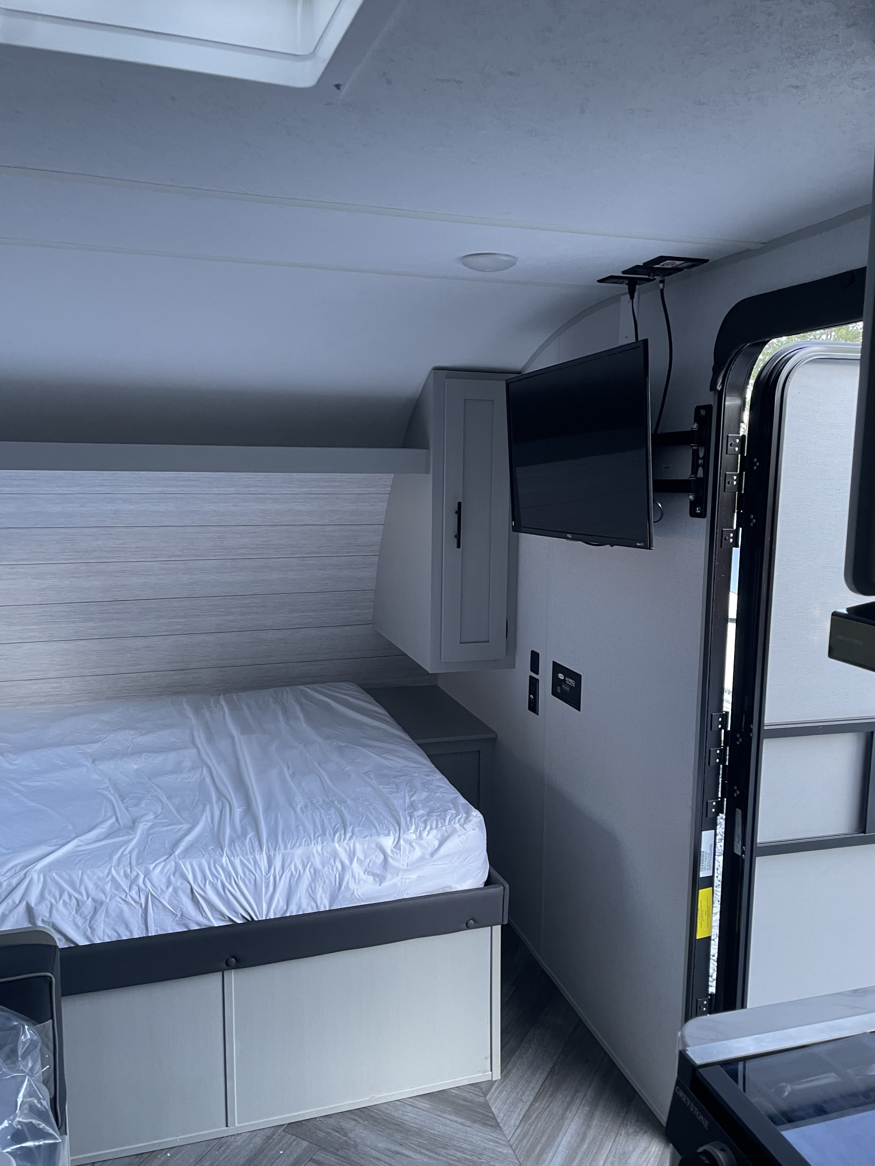 RV rental bedroom showcasing a modern interior with a comfy bed, slatted headboard, wall-mounted TV, and storage cabinet.. Forest River Wildwood FSX 2023