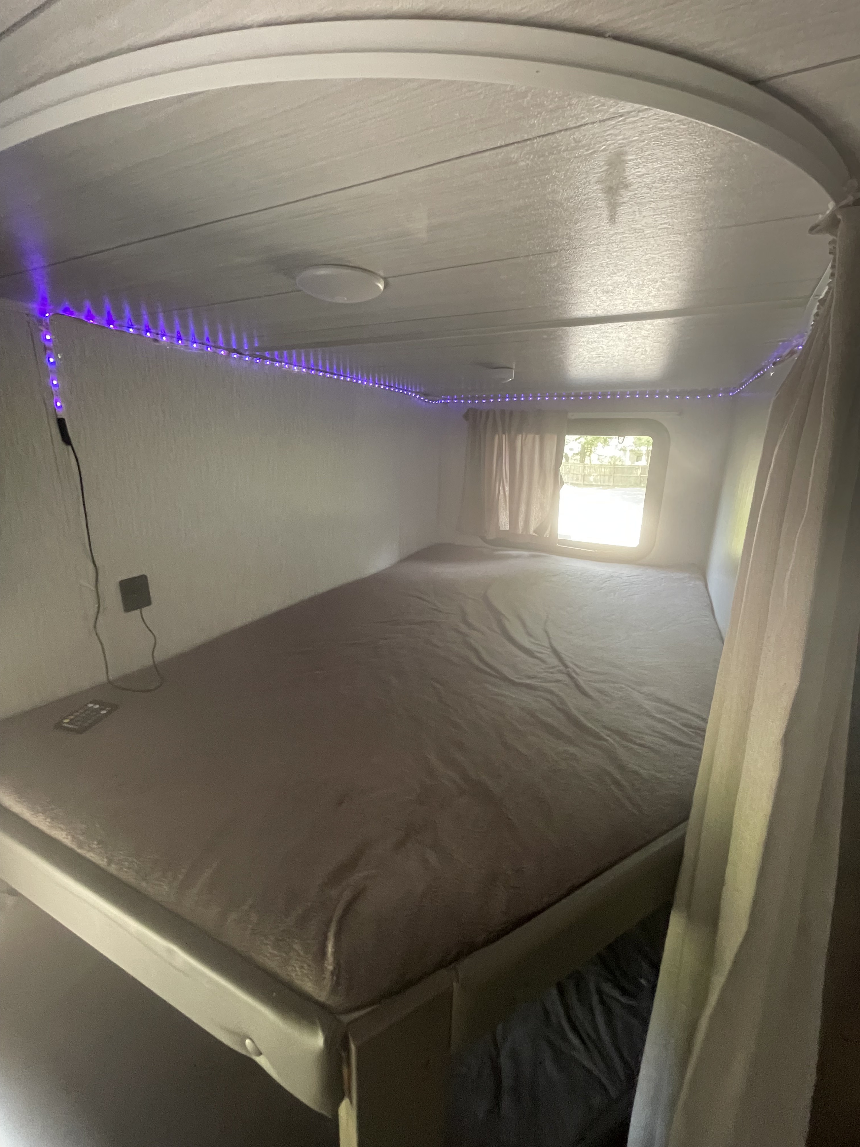 Spacious RV rental bedroom with a large bed, purple LED accent lighting, and window. Ideal for compact living.. Forest River Wildwood X-Lite 2022