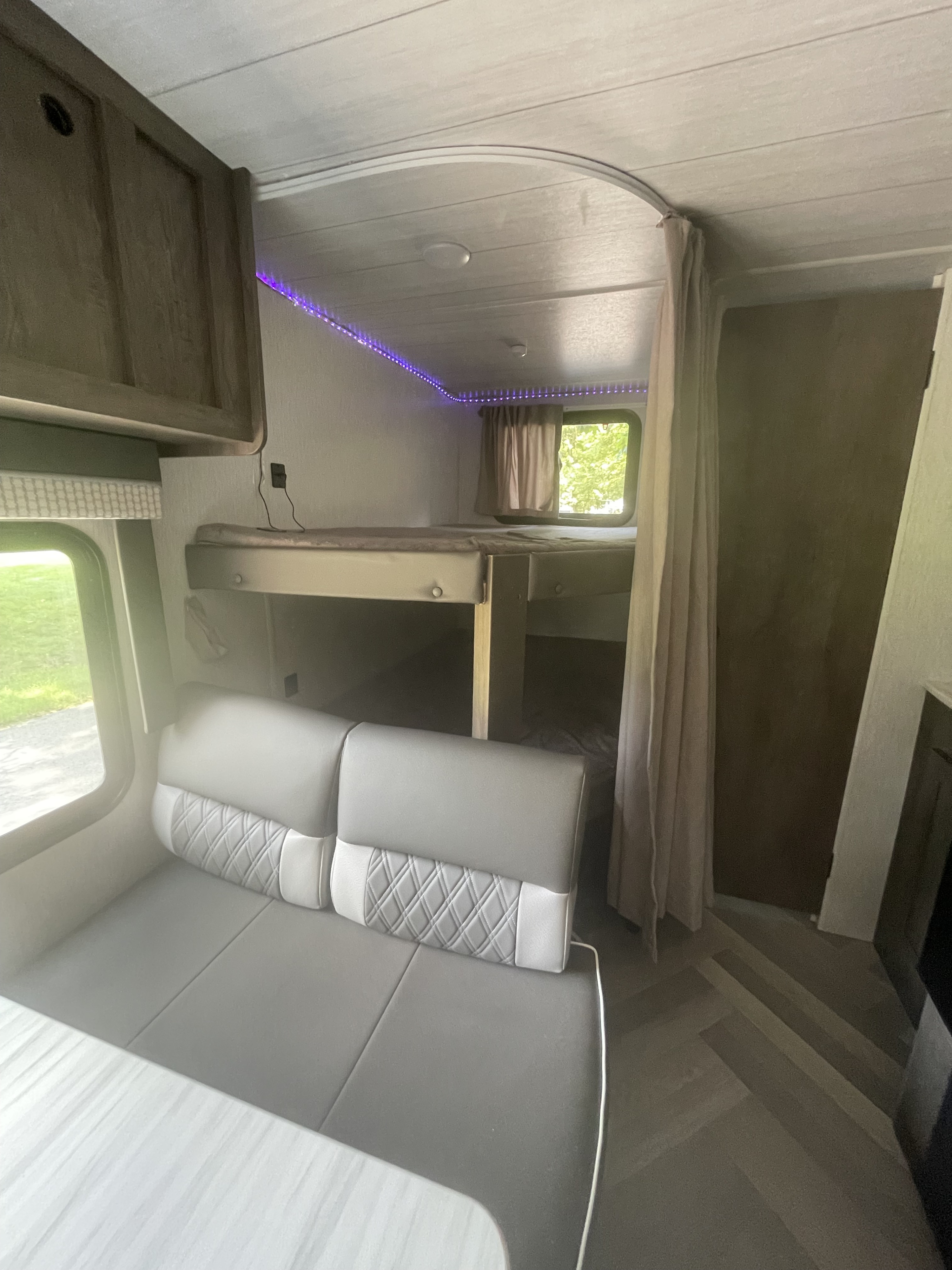 Modern rv rental interior with comfy bunk beds, convertible dinette, window views, and ambient purple LED lights.. Forest River Wildwood X-Lite 2022