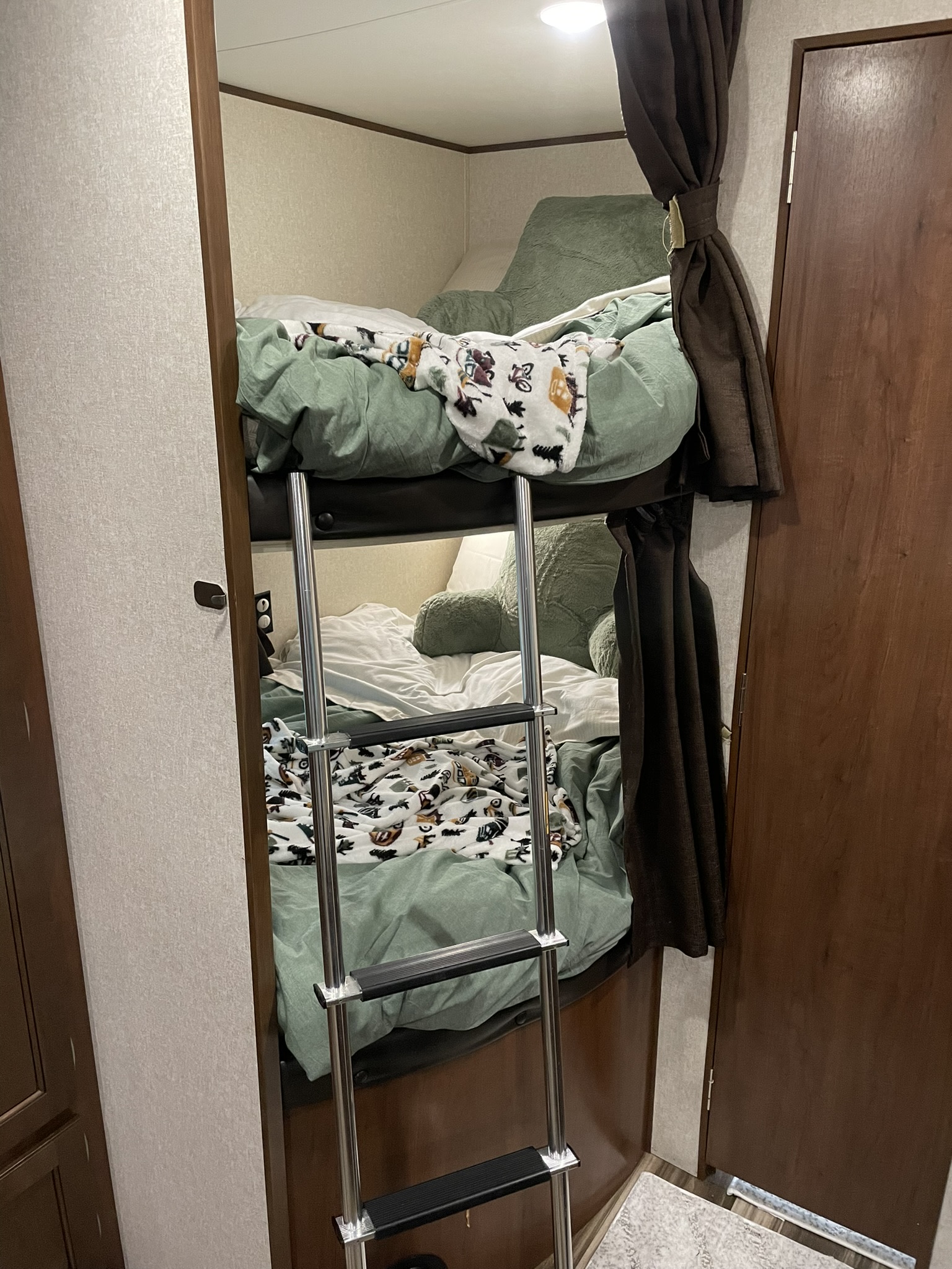 An RV rental's interior shows stacked bunk beds with a ladder, green bedding, and patterned throw blankets.. Jayco Jay Flight SLX 2017