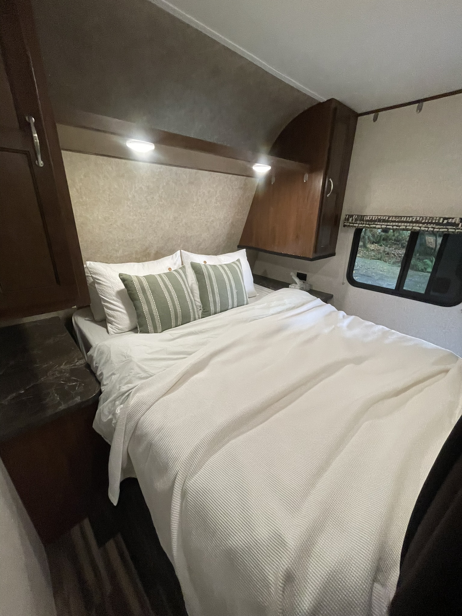 Inviting RV rental bedroom with white bedding, striped pillows, overhead storage, and warm lighting for a cozy stay.. Jayco Jay Flight SLX 2017