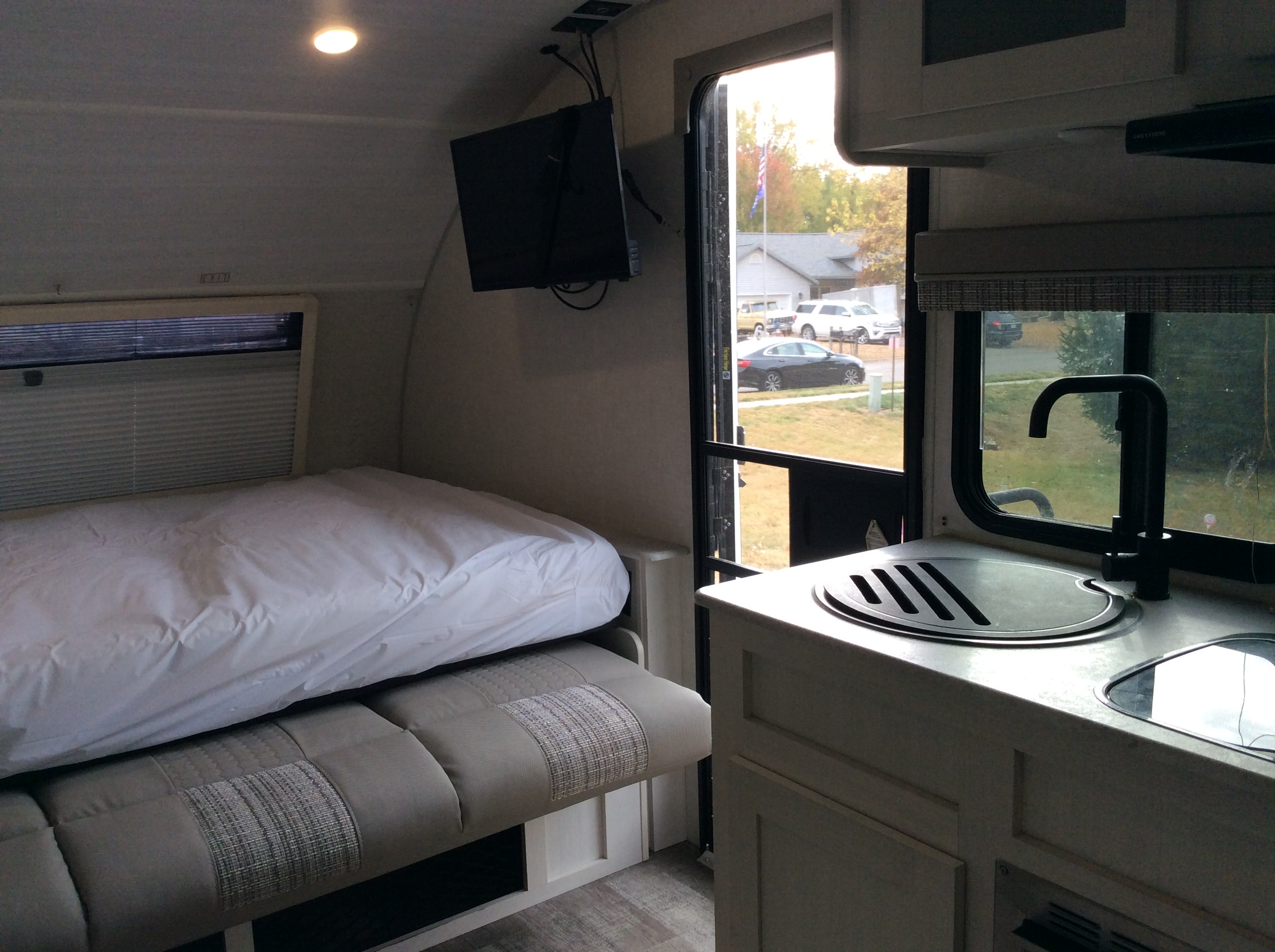 RV rental interior with a cozy bed, compact kitchen featuring a sink, and a wall-mounted TV. The door is open to the outside view.. Forest River R-Pod 193 2021