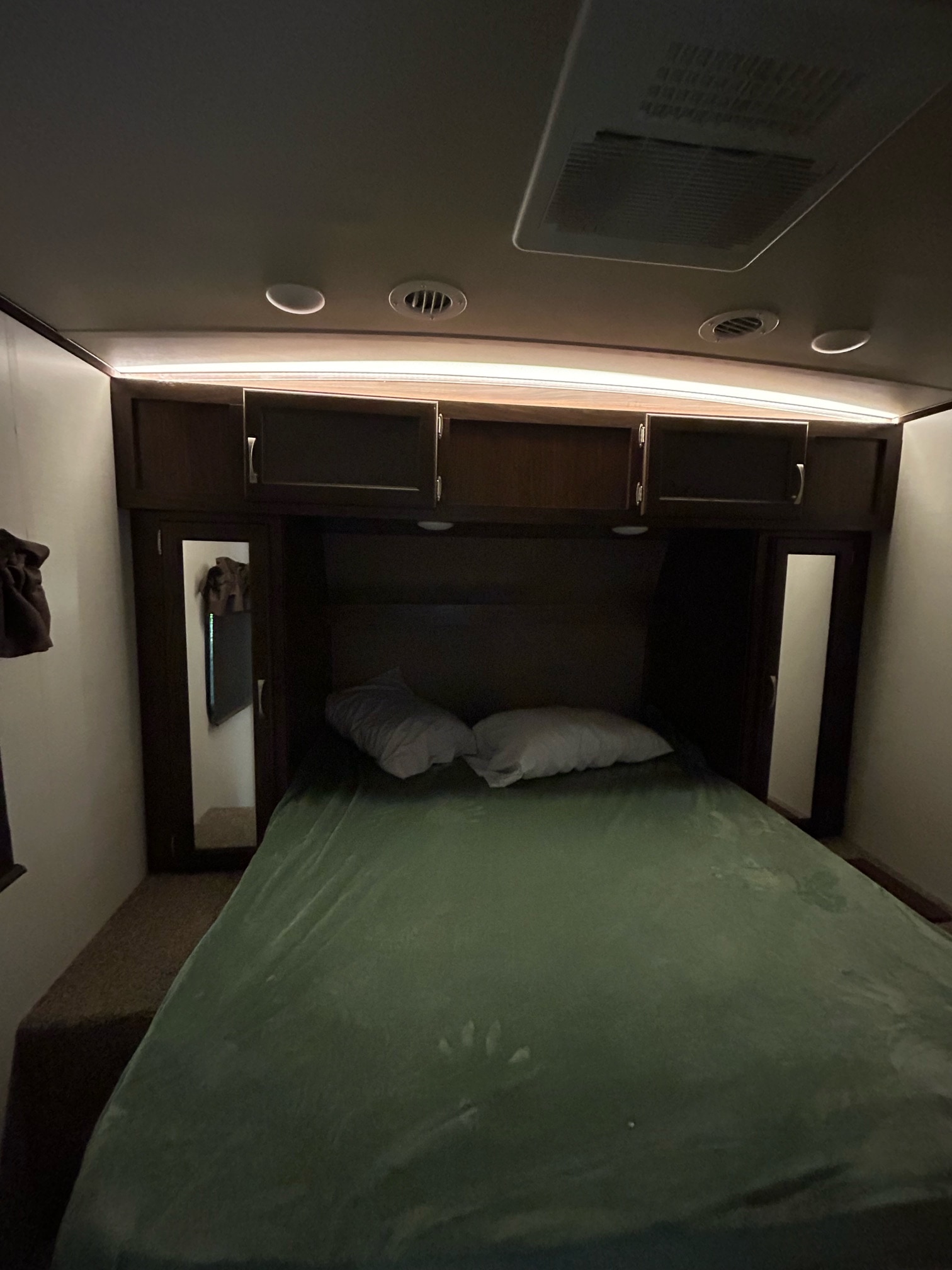 Cozy RV rental bedroom featuring a comfortable bed, wood cabinets, ceiling AC vents, and ambient lighting.. Palomino Solaire 2018