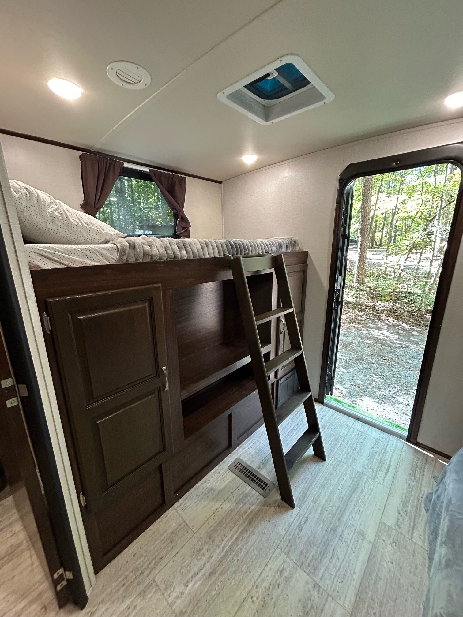 Inside an RV rental, a bunk bed with ladder, storage, and an open door reveals a wooded campsite view.. Palomino Solaire 2018