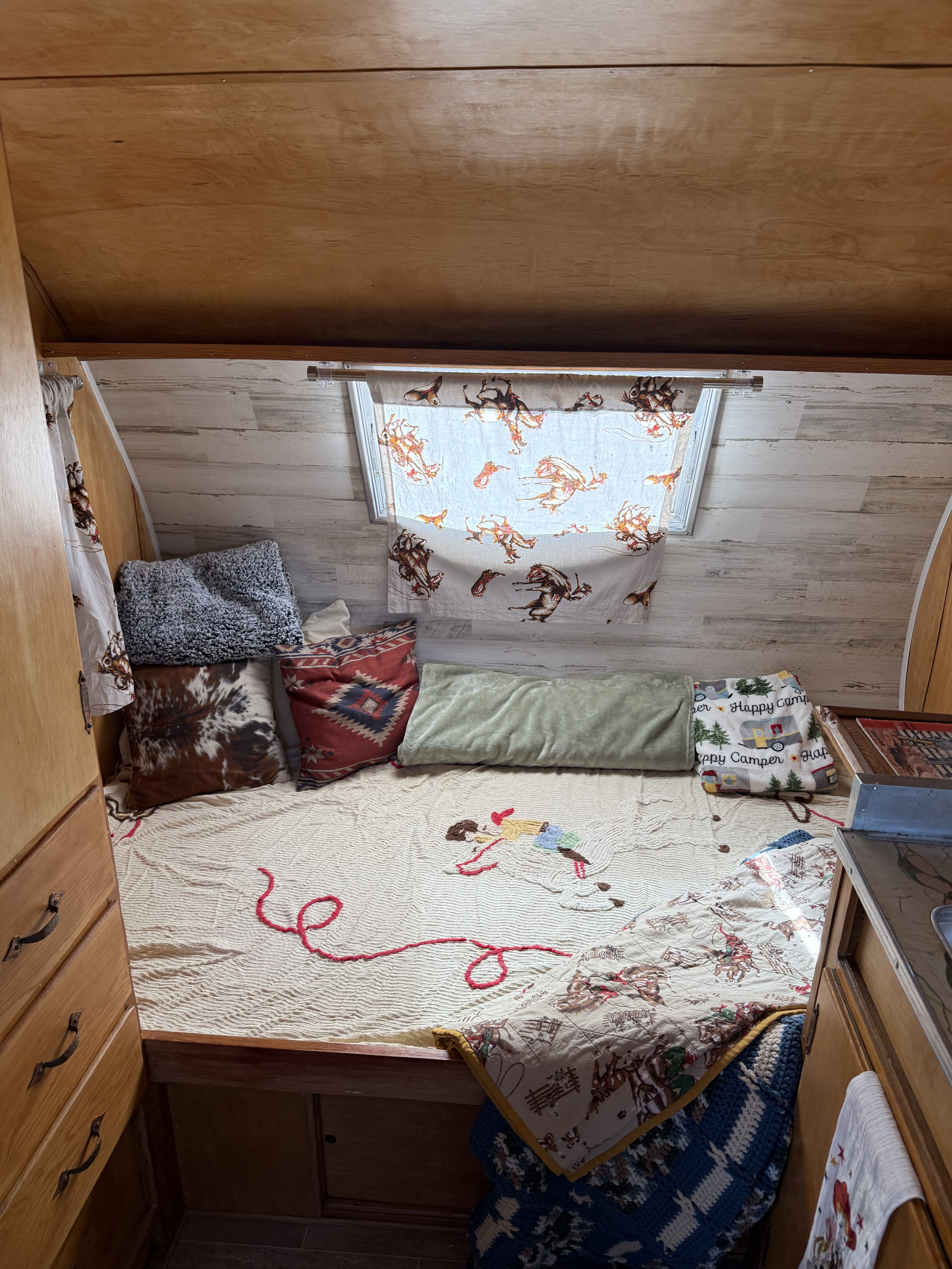 Cozy RV rental interior with western-themed bedding, a bed, and wooden cabinetry, creating a comfortable travel space.. Custom Camper 1959