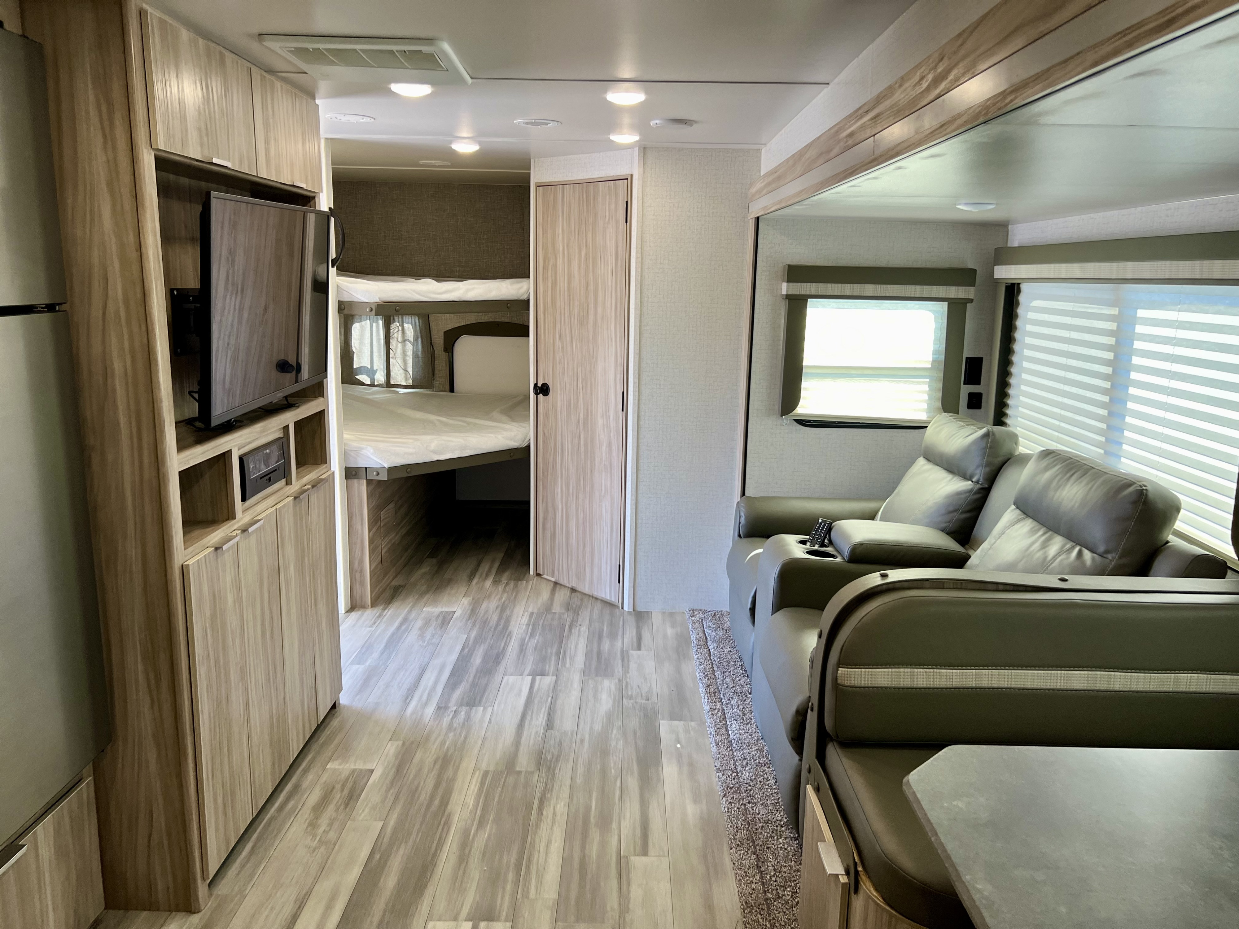 Modern rv rental interior: living area with recliners, entertainment center, fridge, bunks, and dining space.. Winnebago Minnie 2021
