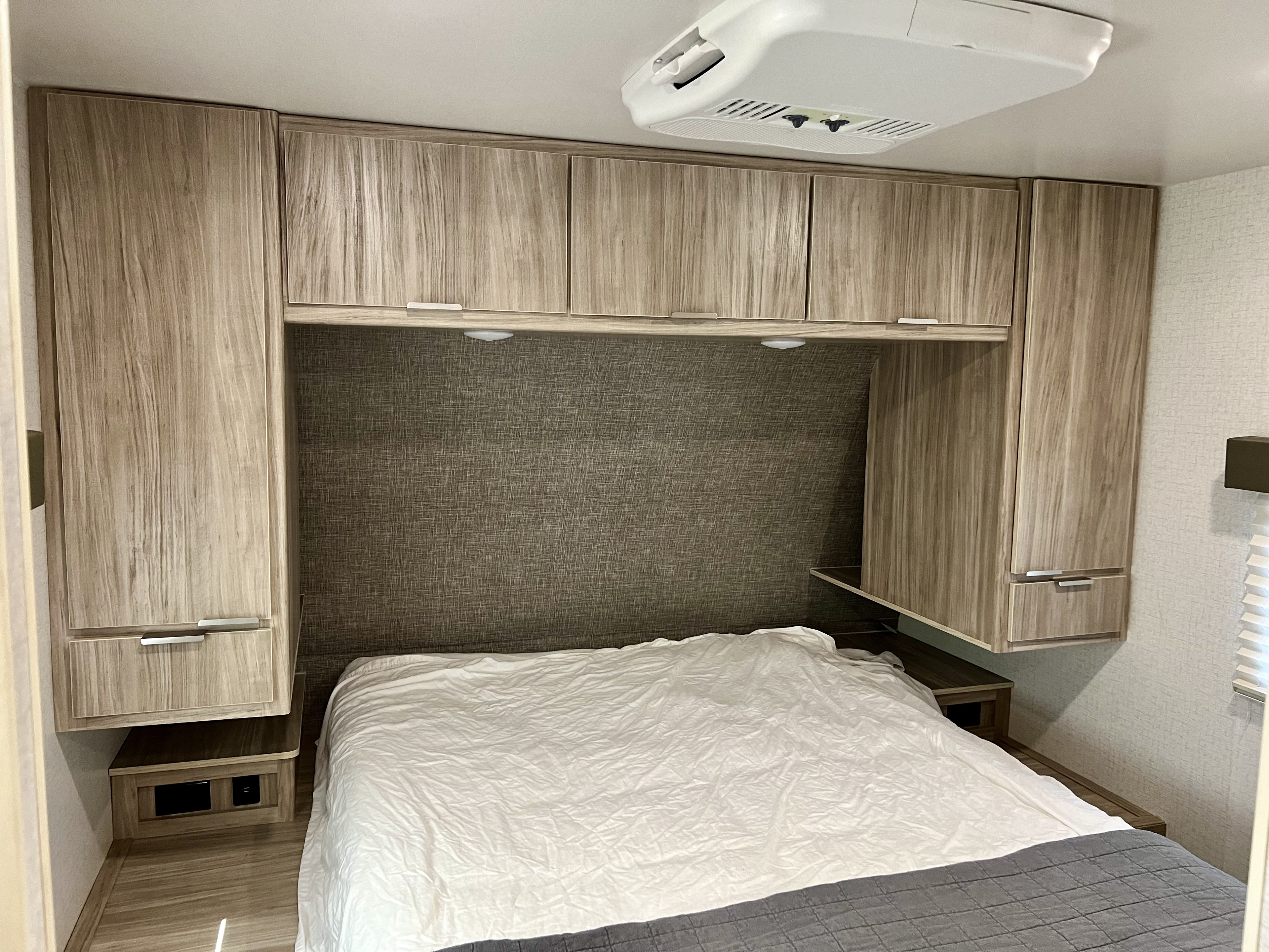 RV rental bedroom featuring a comfortable bed, numerous wooden storage cabinets, and a ceiling-mounted AC unit.. Winnebago Minnie 2021