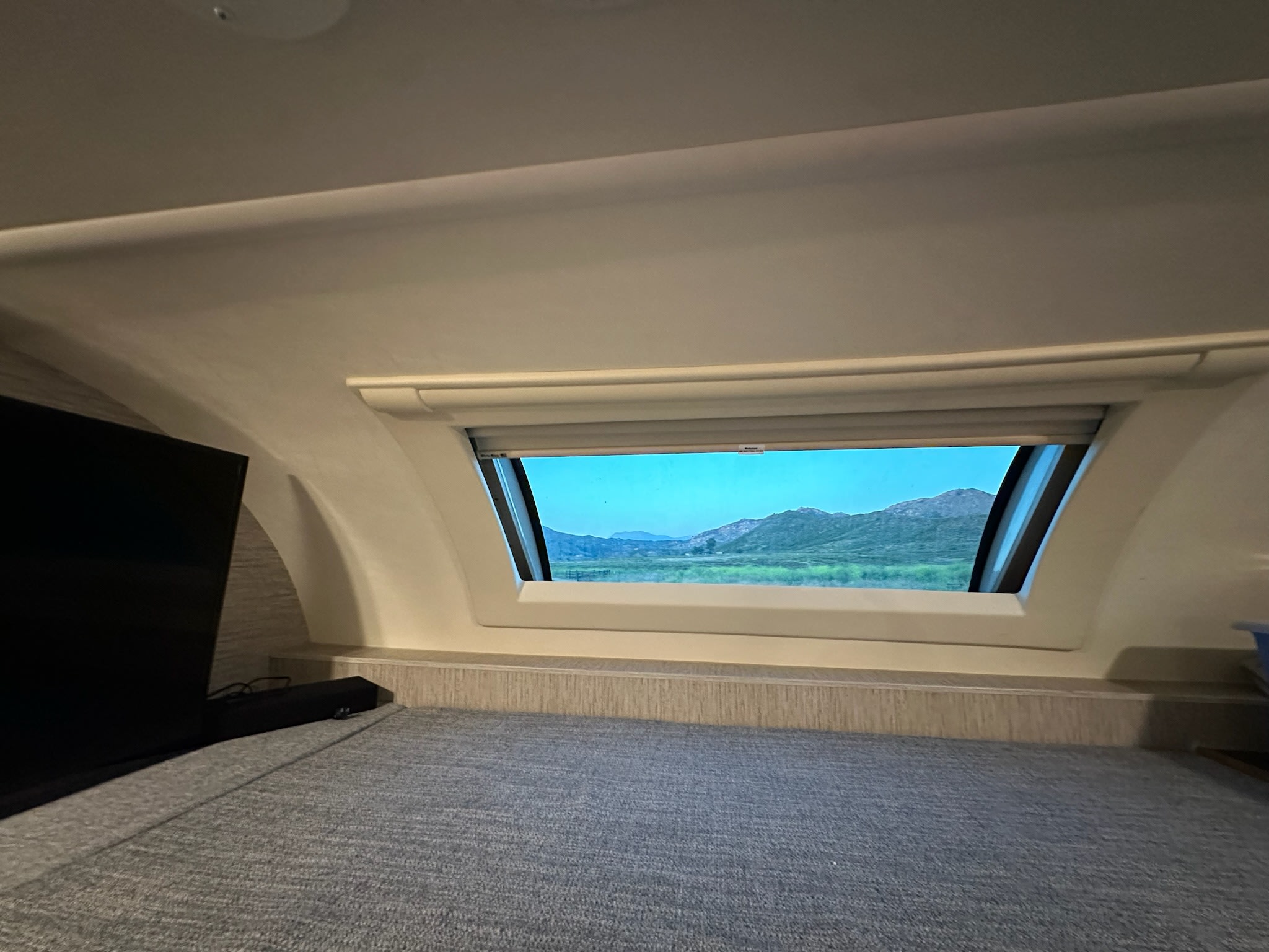 Wake up to nature! This RV rental bedroom offers a comfortable bed, TV, and panoramic window view of mountains and fields.. Thor Quantum 2021