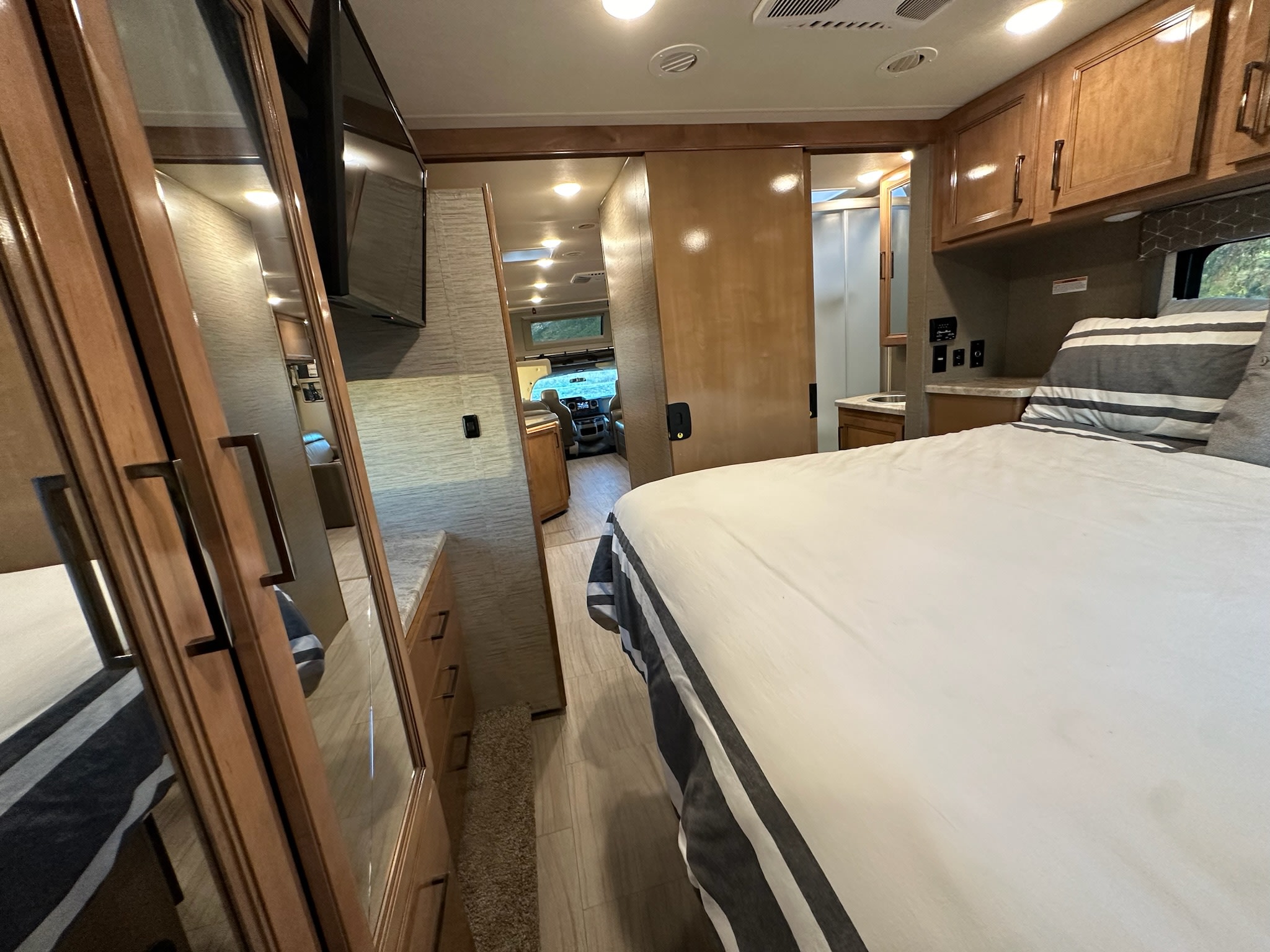 RV rental: Bright RV interior showing a bed with striped bedding, mirrored wardrobe, bathroom & front.. Thor Quantum 2021