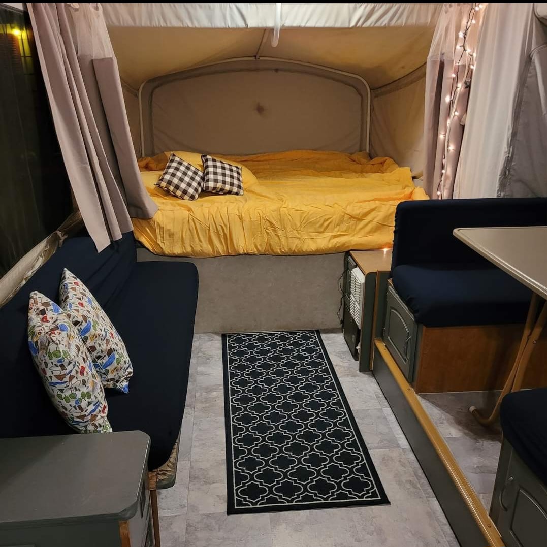 Cozy RV rental interior featuring a comfy bed with yellow bedding, blue couch, dining area, and decorative rug for travel.. Fleetwood UTAH 2005