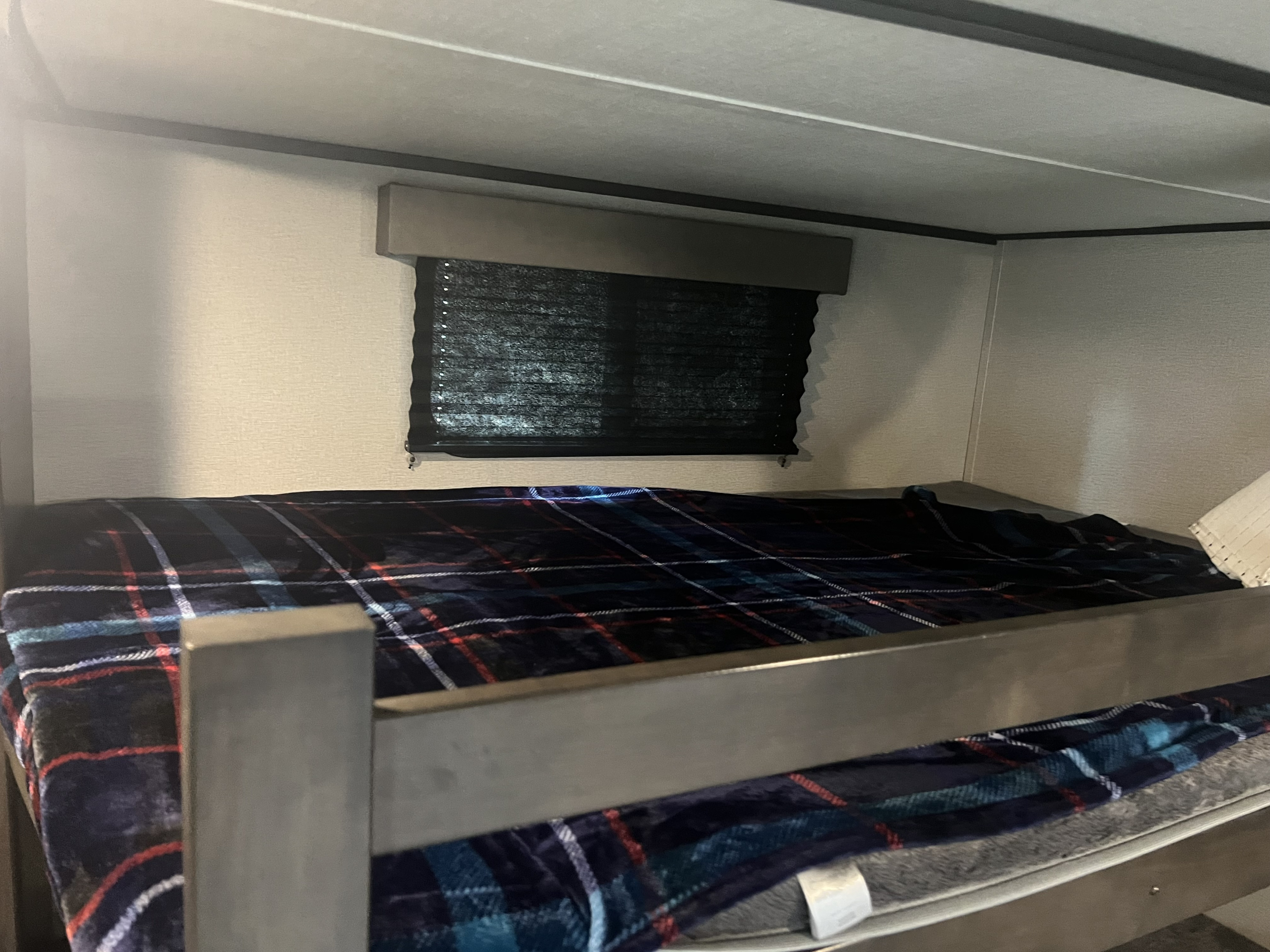 Cozy RV rental bunk bed with a dark plaid blanket and window blind, providing a compact sleeping area.. Grand Design Transcend 2021