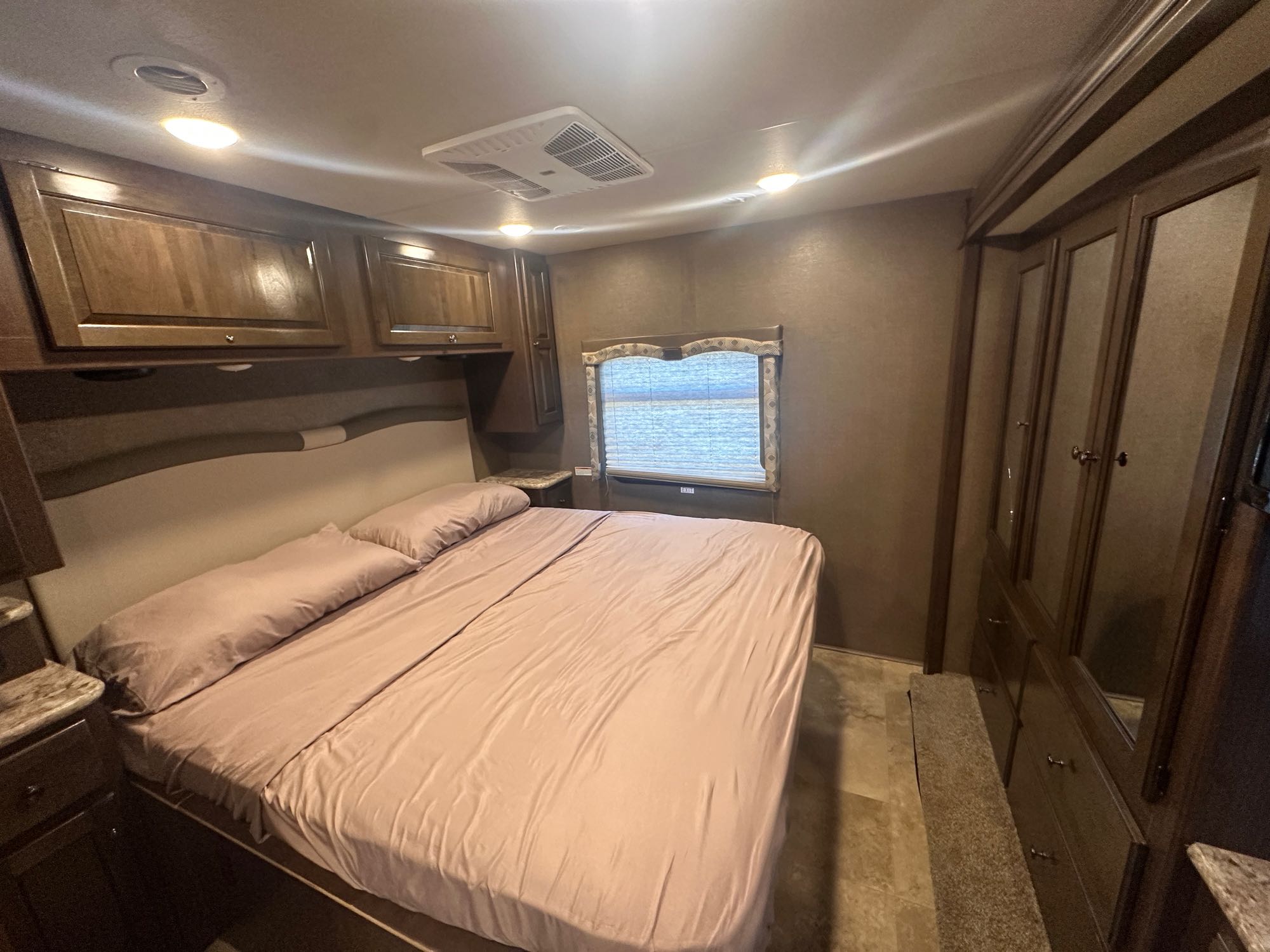 Cozy RV rental bedroom featuring a comfortable bed, built-in overhead cabinets, and a full wardrobe. Perfect for travelers seeking comfort.. Thor Windsport 2018