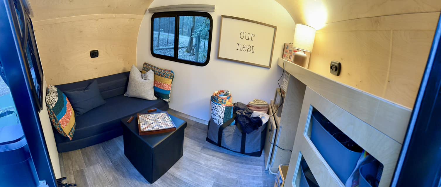 Cozy RV rental interior: sofa, Scrabble, "Our Nest" sign, and nature views through the window.. Rustic Trails Koala 2023