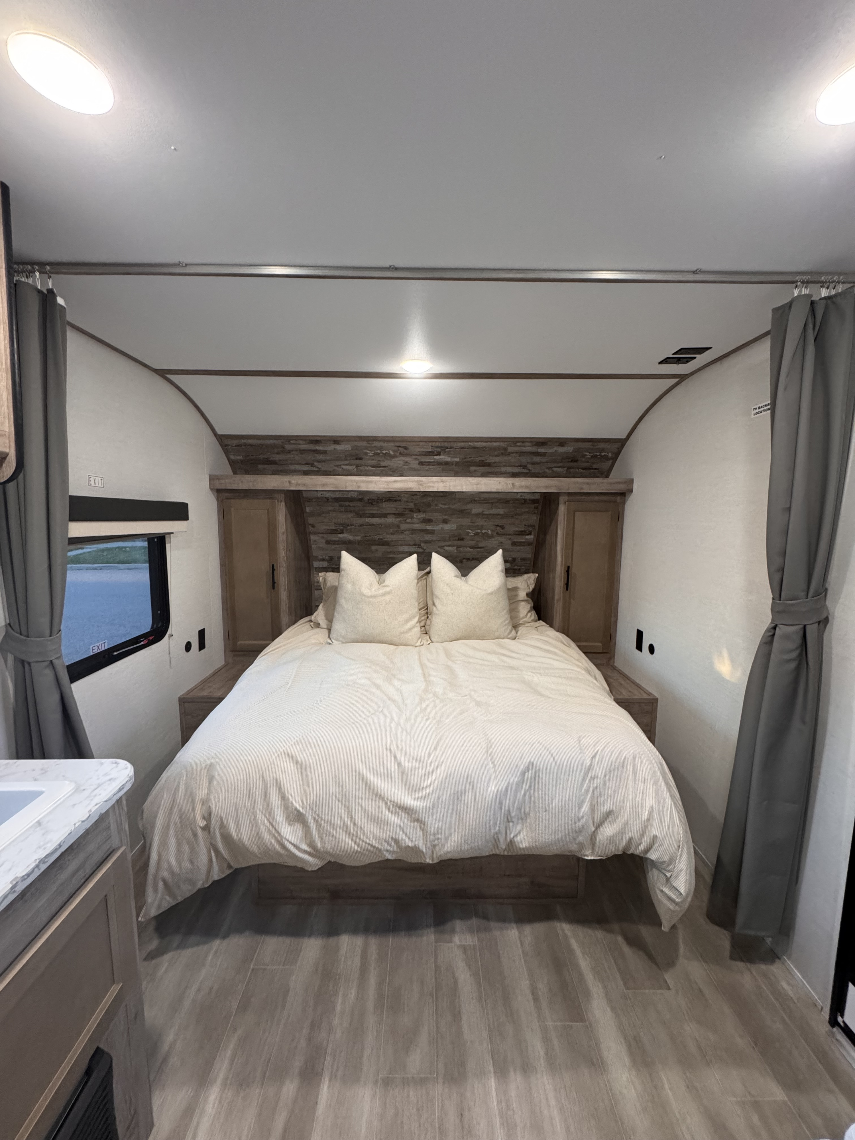 Modern RV rental bedroom with a comfortable bed, stylish wood headboard, and window view. Ideal for adventures.. Grand River 25BH 2025