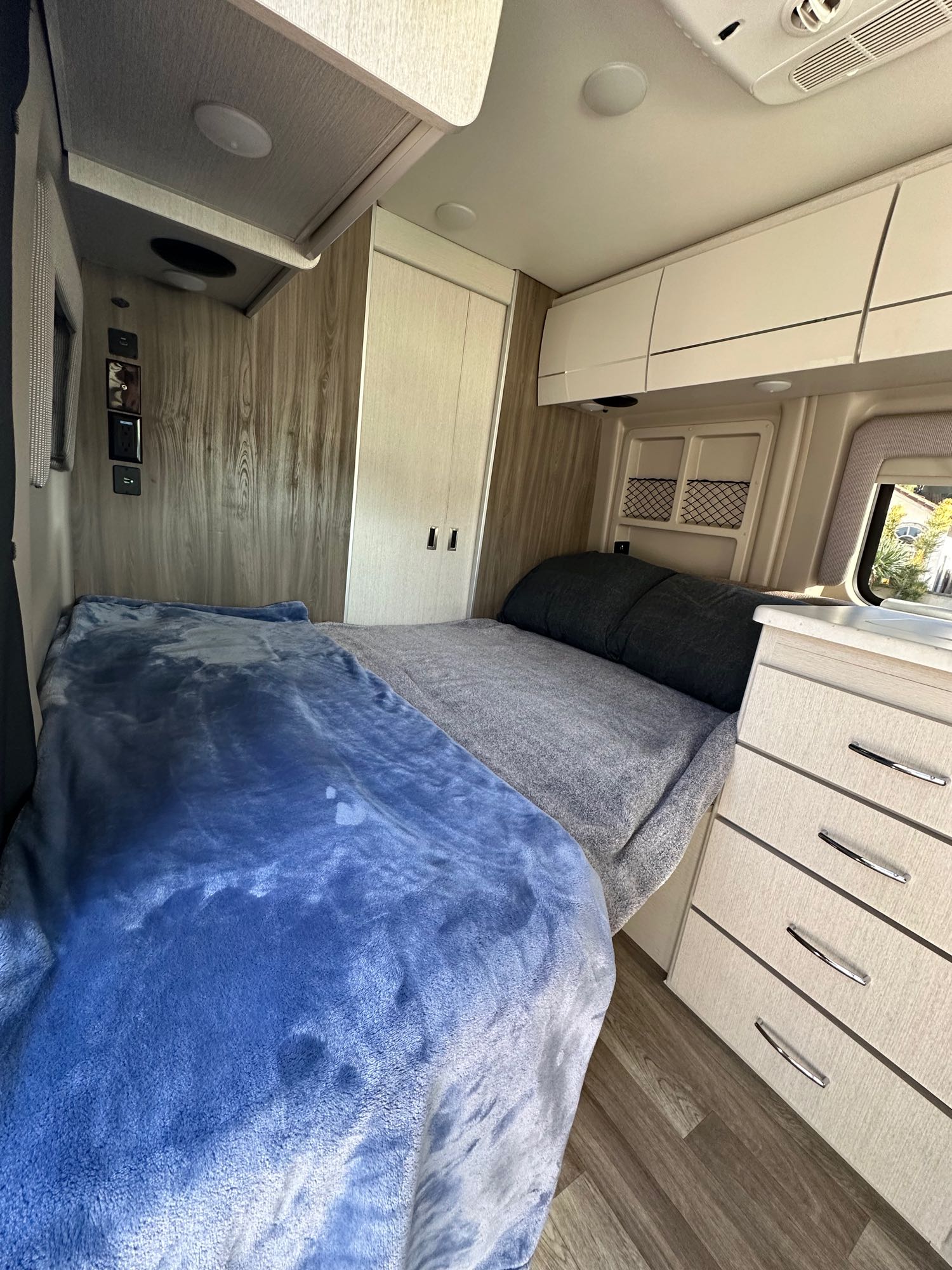 RV rental interior features two cozy beds, sleek overhead storage, a dresser, and wood accents, providing a comfortable travel space.. Thor Rize 2023