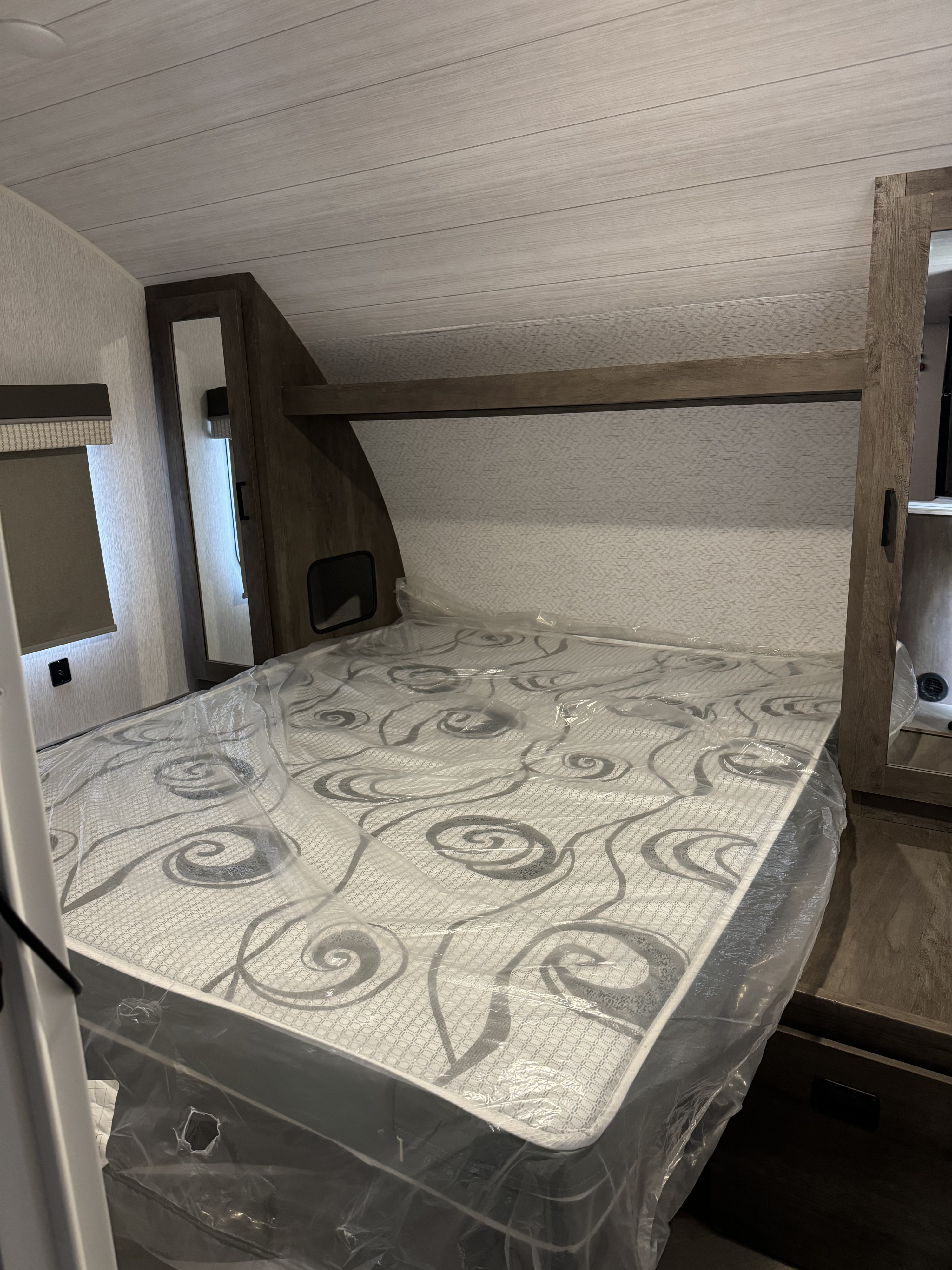 RV rental bedroom: New mattress (in plastic), built-in storage, mirrored closets, and light-toned, paneled interior.. Forest River Wildwood X-Lite 2022