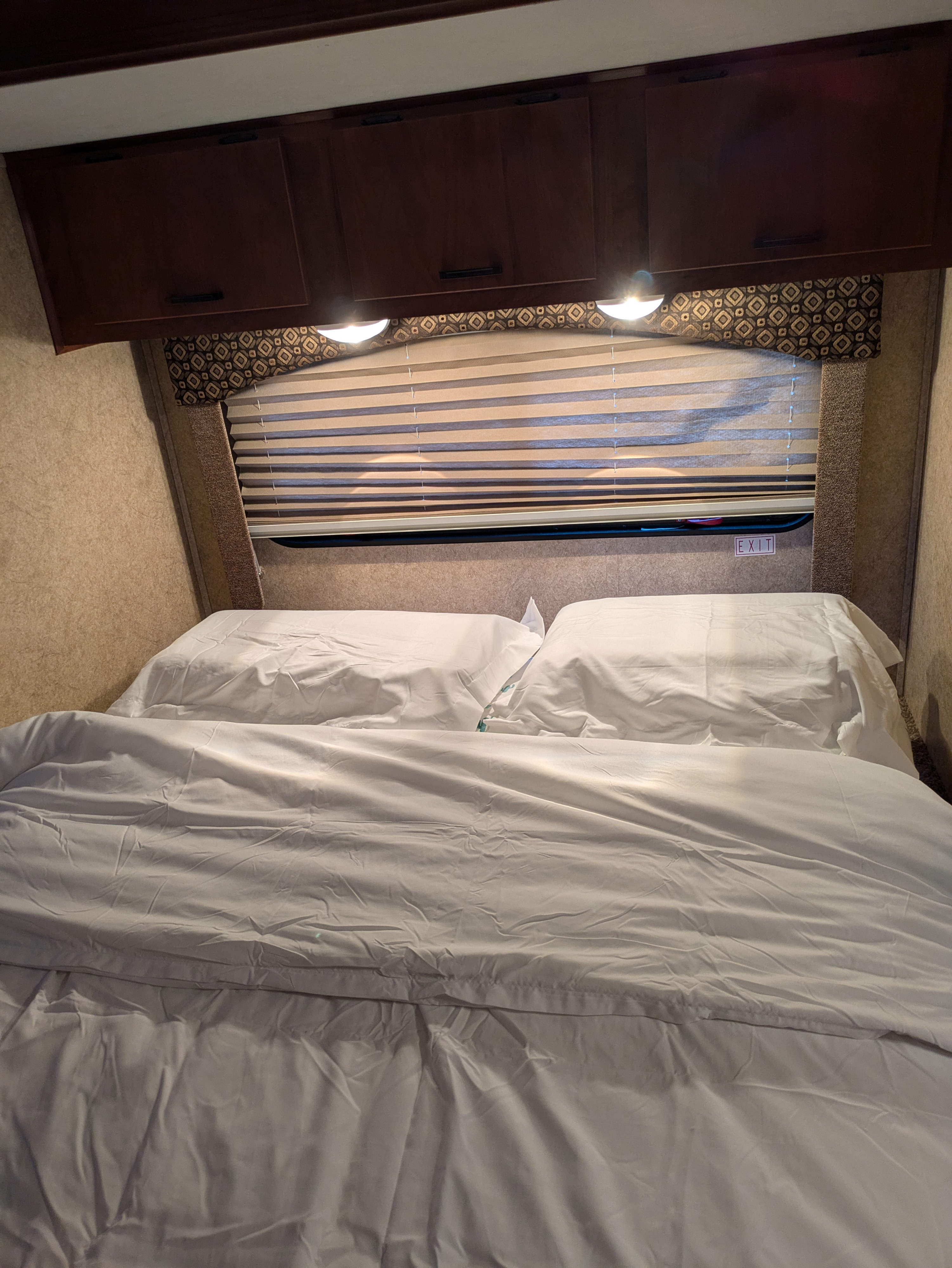 Cozy RV rental bedroom with white bedding, overhead cabinets, and a window with blinds. Ideal for travel.. Forest River Sunseeker LE 2012