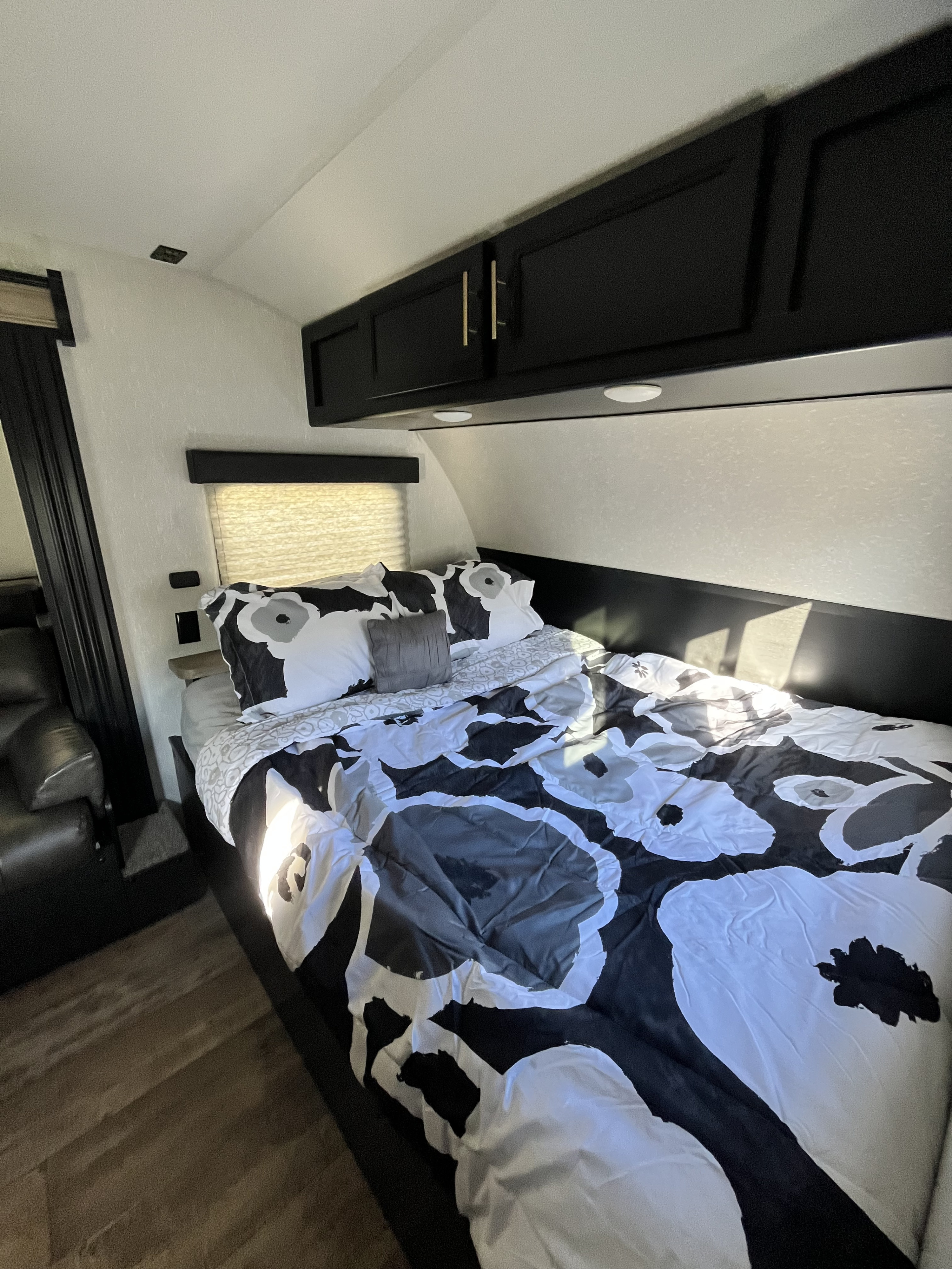 Comfortable RV rental bedroom with modern black and white floral bedding, overhead cabinets, and wood flooring.. Forest River Cherokee Wolf Pup 2021