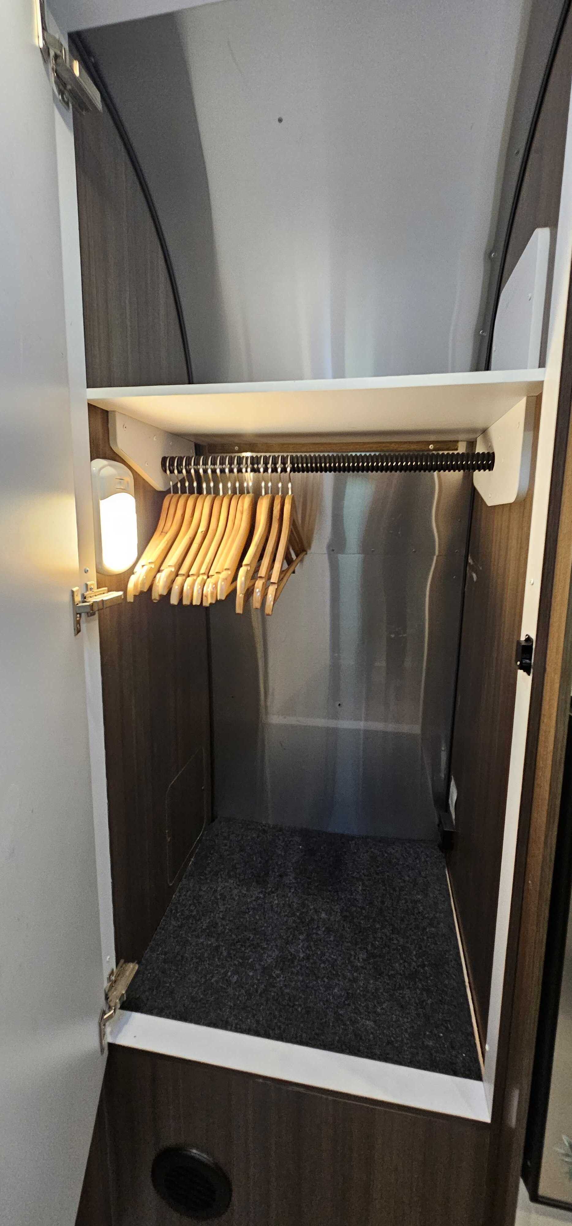 Inside an rv rental: a compact, lit closet with wooden hangers on a rod and a shelf, providing smart storage for travel.. Airstream Caravel 2022