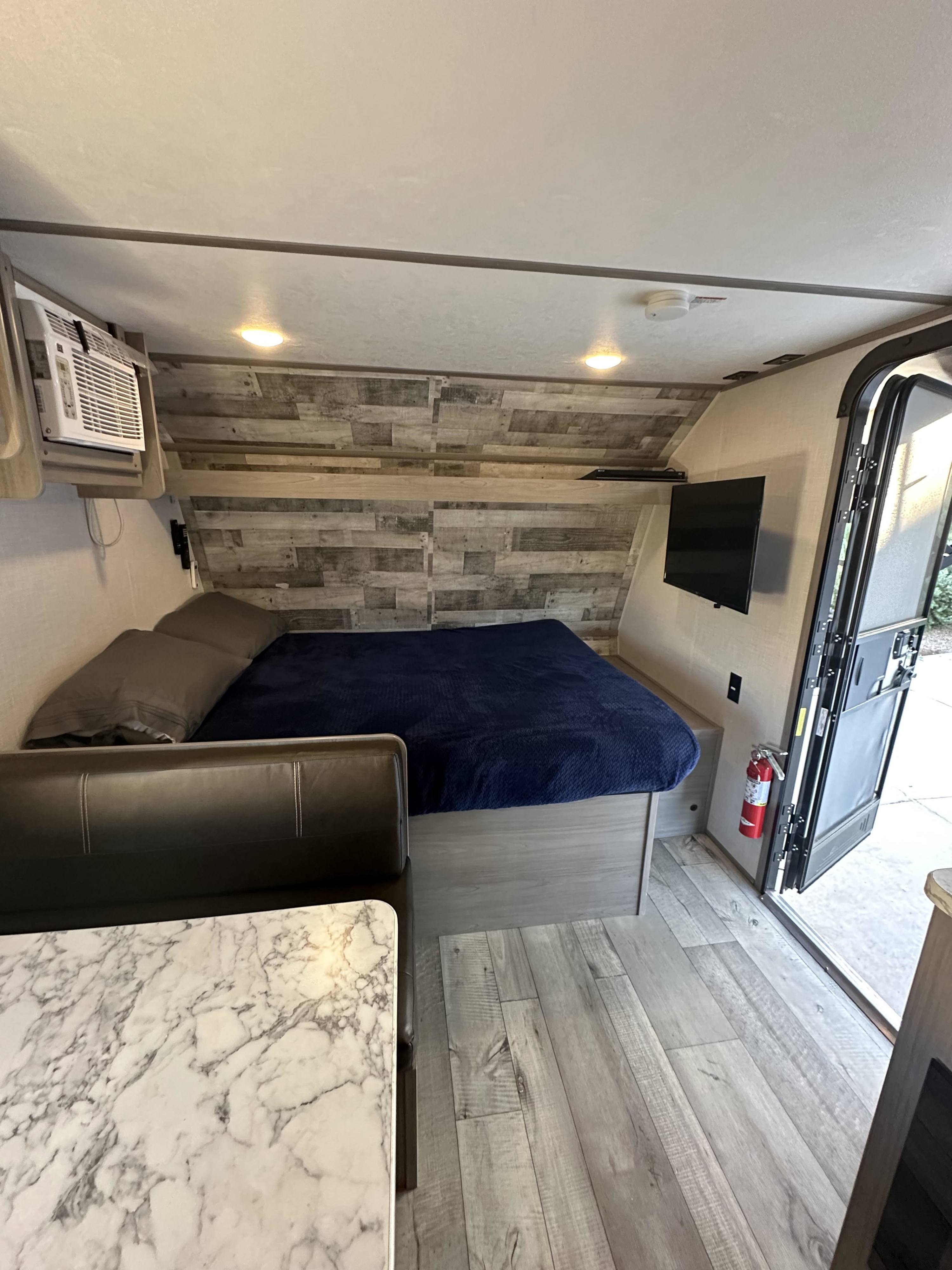 Compact RV rental interior: bed, TV, AC unit, dining area with marble table, and fire extinguisher.. Dutchmen Coleman Lantern LT 2023
