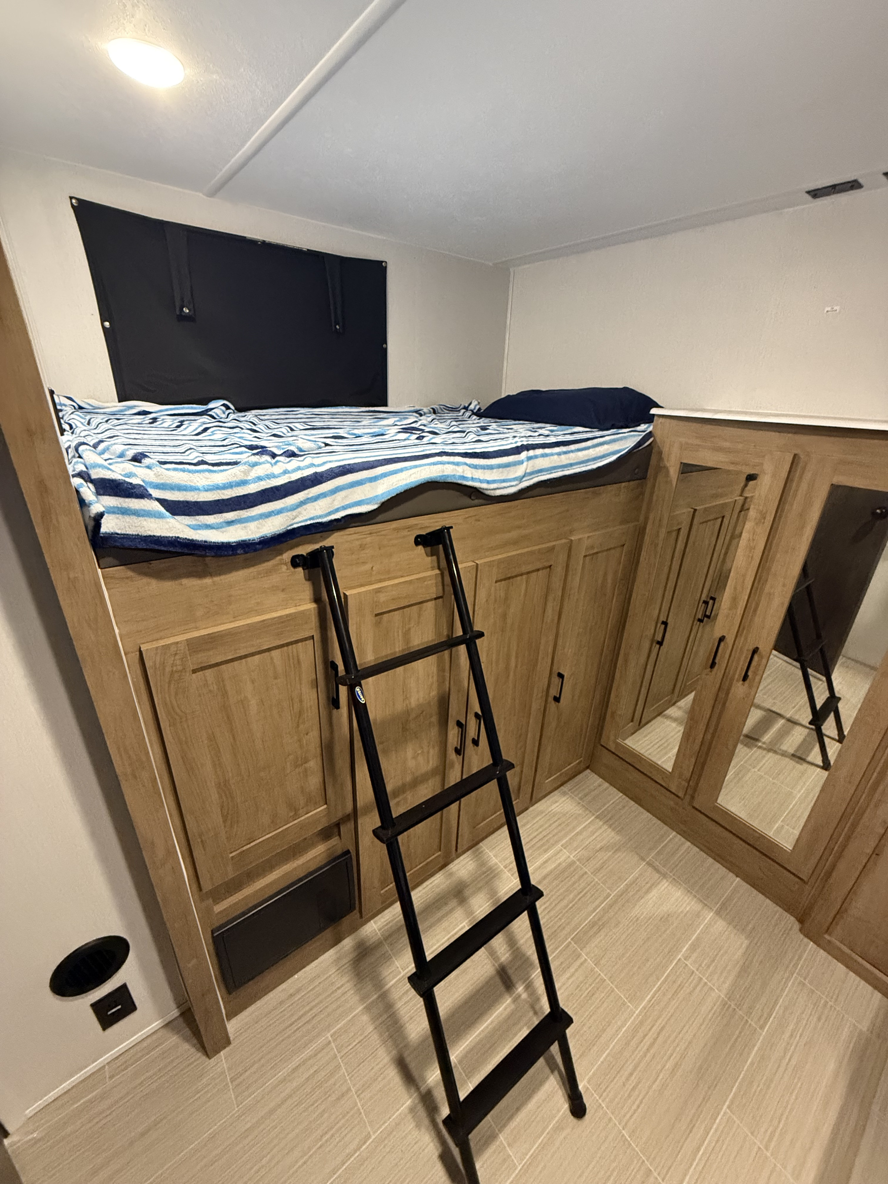 RV rental interior: a bunk bed with striped blanket, black ladder, and wood cabinets with mirrored doors, on tiled floor.. Coachmen Express 2024