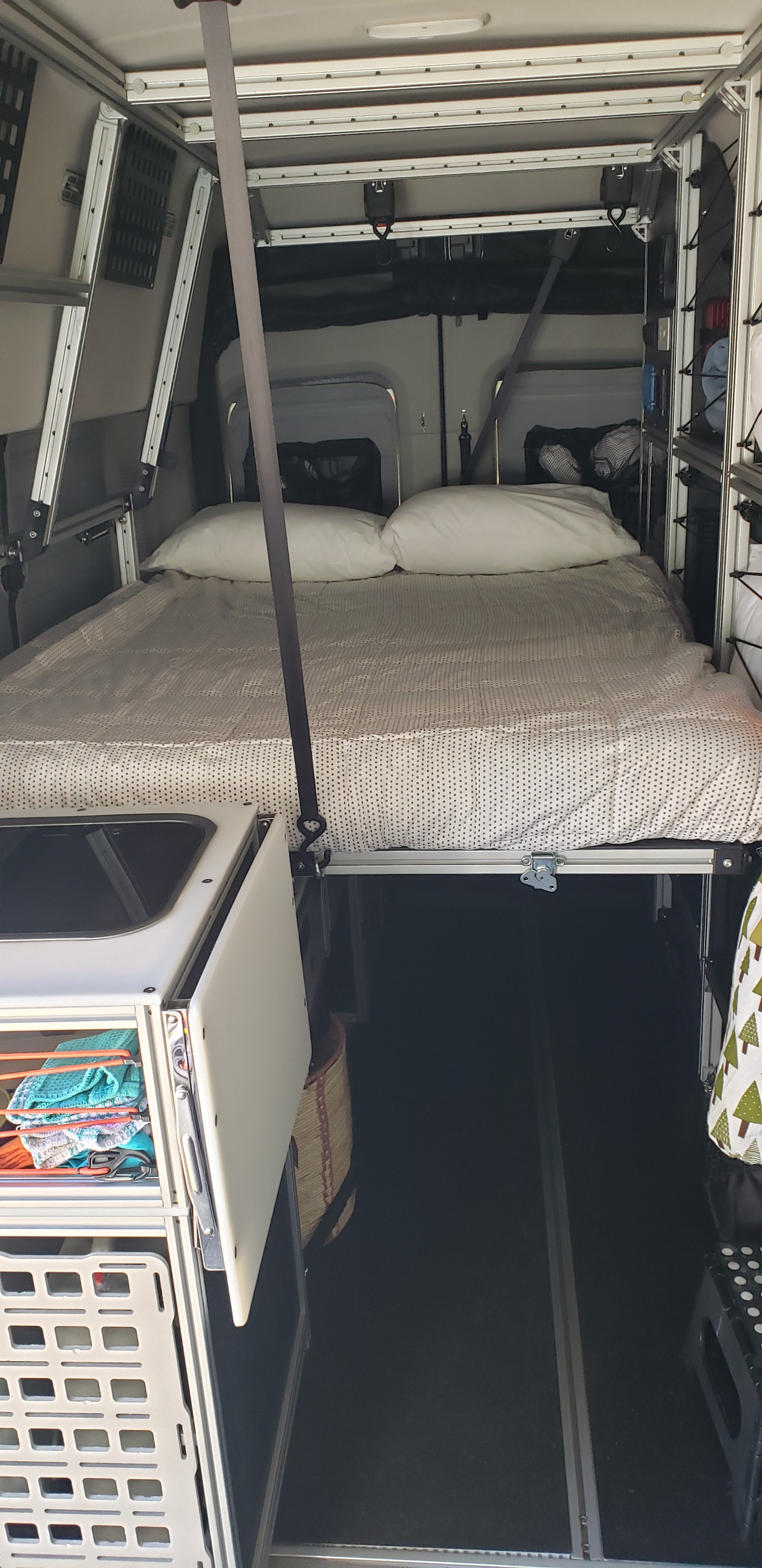 This RV rental showcases a modular camper van interior with an elevated bed, storage units, and open floor space below.. Ford Transit Custom 2019
