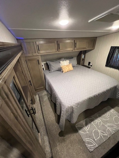 Cozy RV rental bedroom featuring a queen bed with overhead cabinets, nightstand, and a soft carpeted floor.. Forest River Cherokee Wolf Pack Toy Hauler 2020