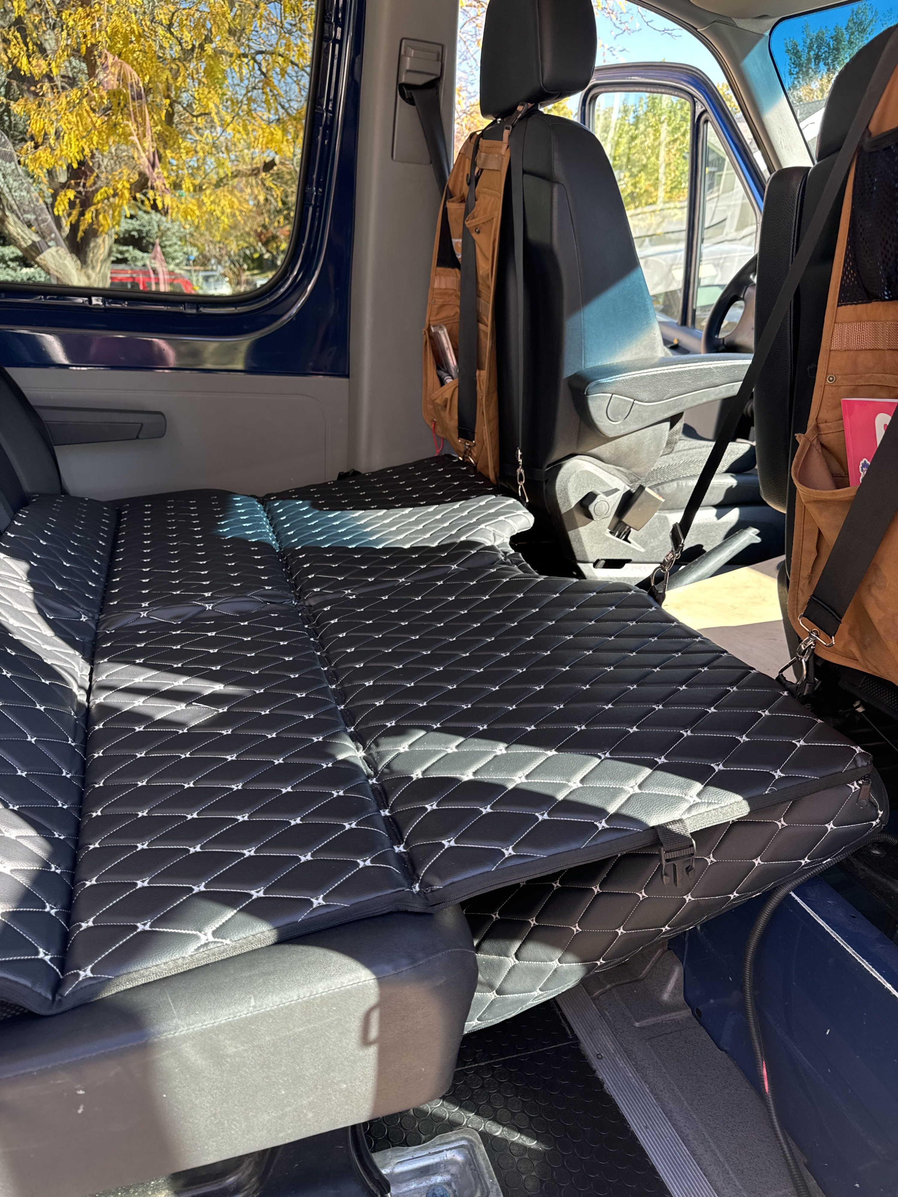 Black quilted mattress fills this RV rental van's interior, showing autumn leaves outside. Ready for adventure!. Mercedes-Benz Sprinter 2016
