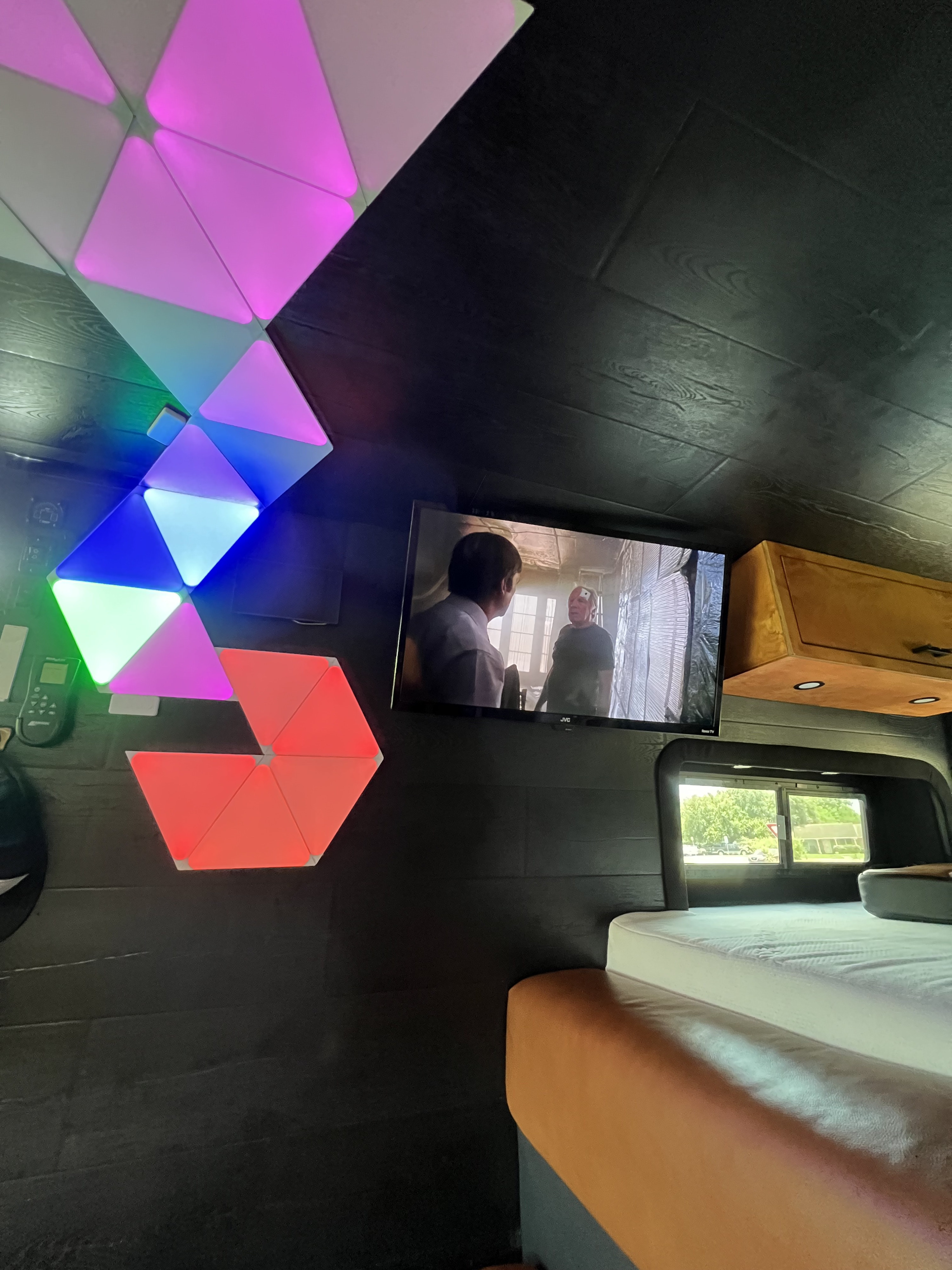 Modern RV rental interior: dynamic triangular LED lights, a TV playing, and a comfortable bed. Perfect for your next adventure.. Mercedes Sprinter 2500 Turbo Diesel 2023