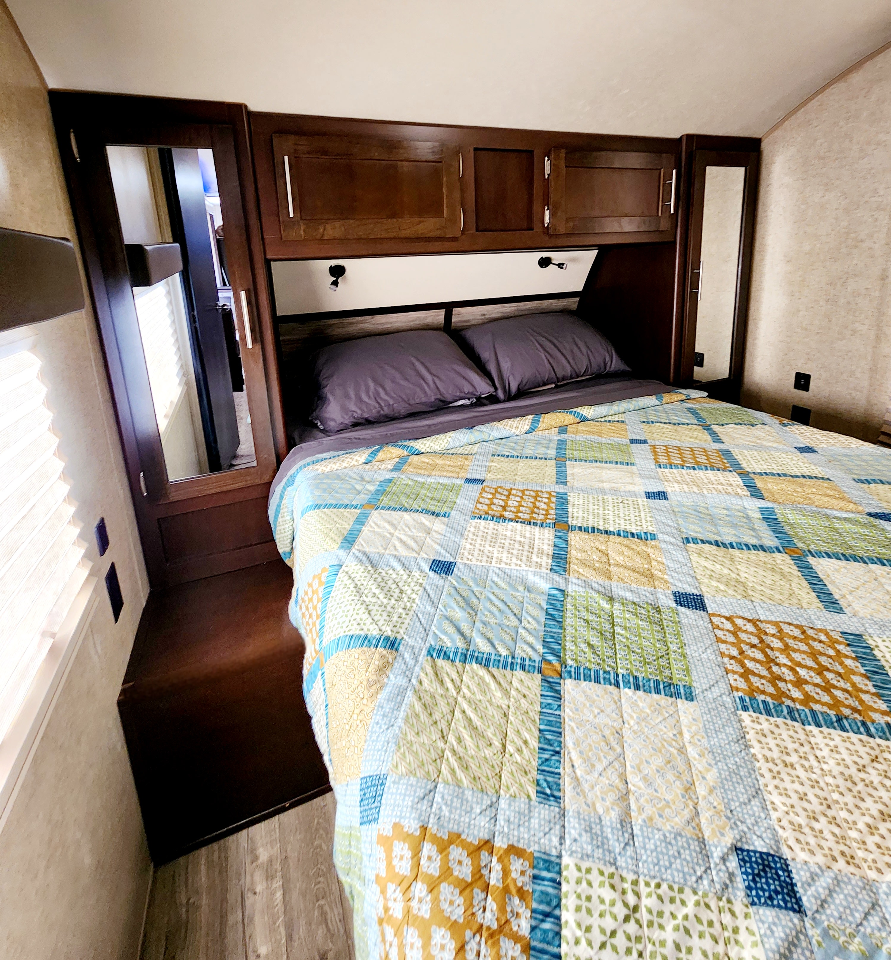 This RV rental bedroom offers a comfortable bed with a lively patchwork quilt and mirrored storage. Cozy travels!. Forest River Cherokee 2018