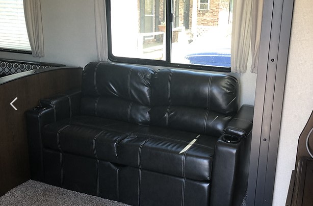 An RV rental's cozy interior features a black leather sofa with cup holders by large windows.. Prime Time Avenger ATI 2019